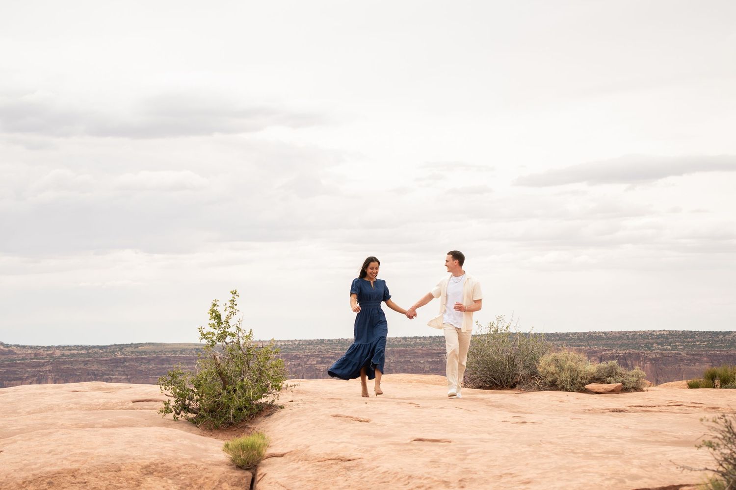 Couple holding hands and walking together across a red rock overlook at Dead Horse Point
