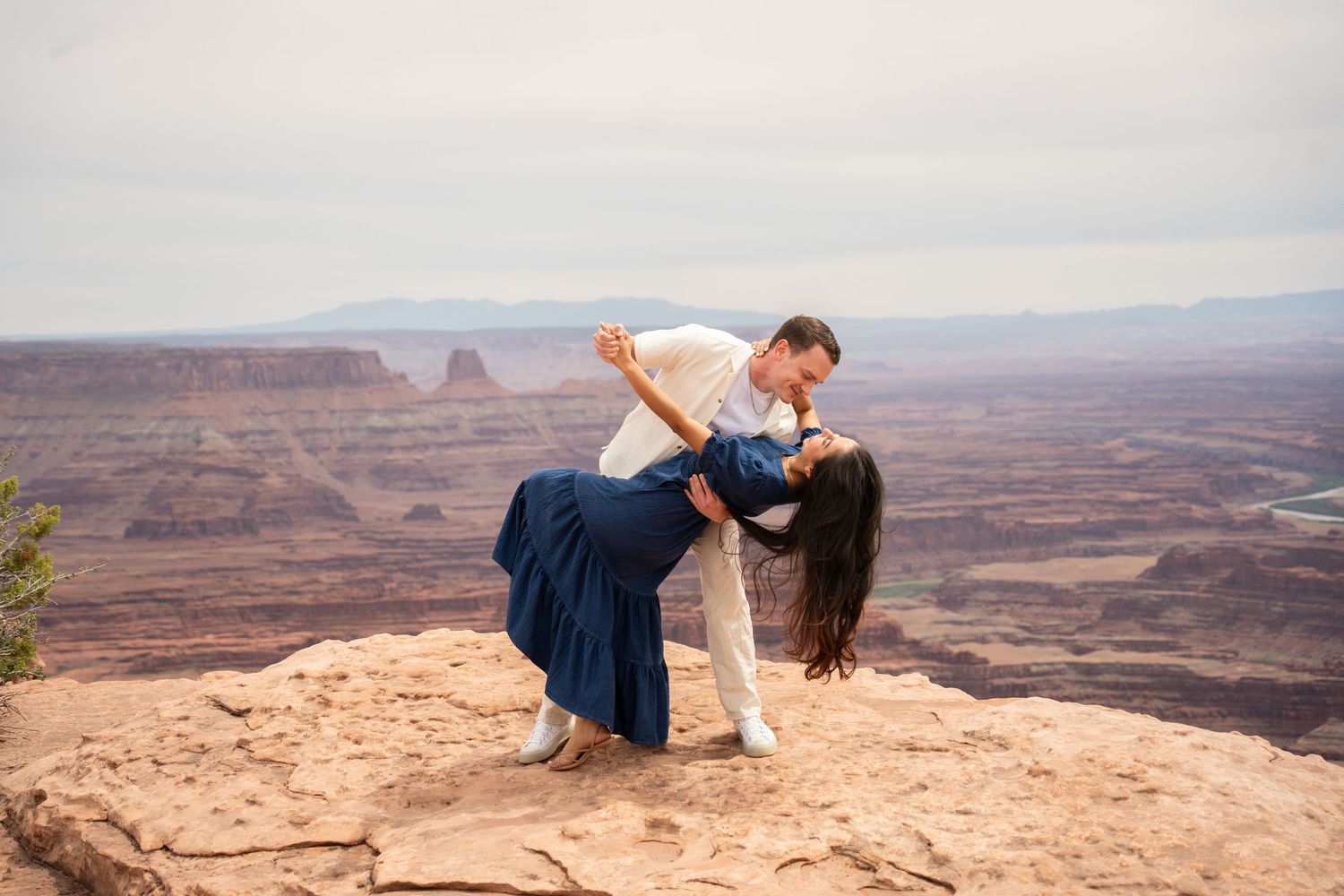 Couple dancing and dipping on a red rock overlook with the canyon and Colorado River spread out behind them