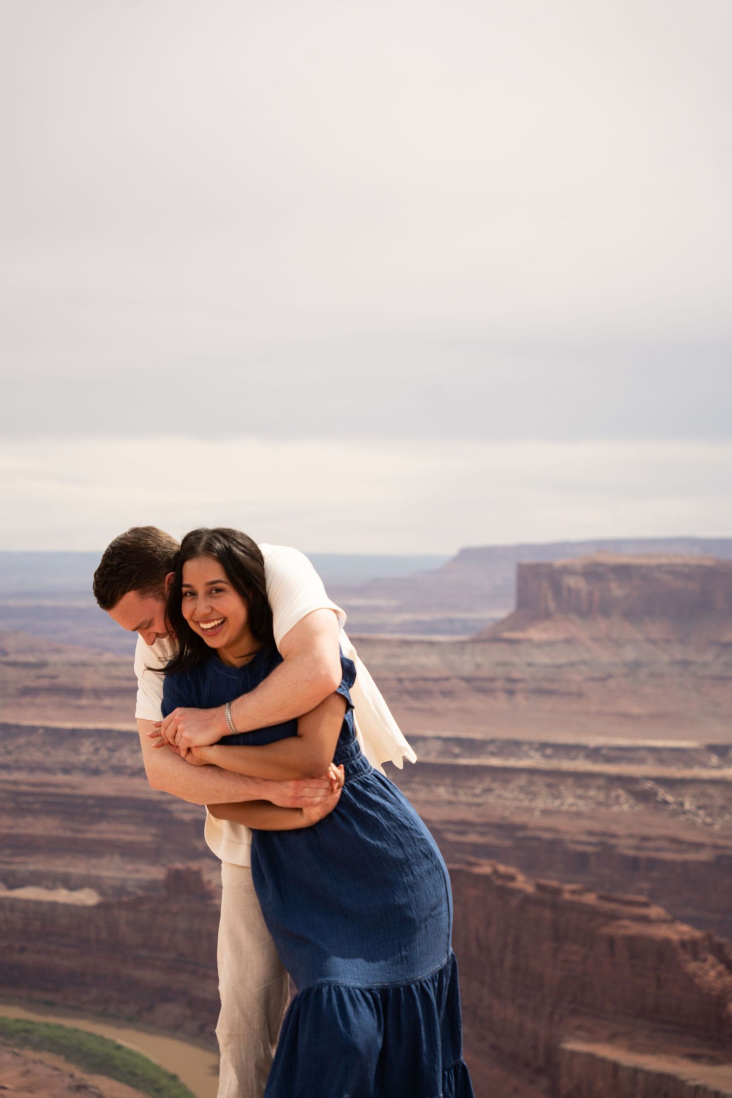 Couple embracing and laughing at a canyon overlook above Canyonlands, red rock landscape behind them