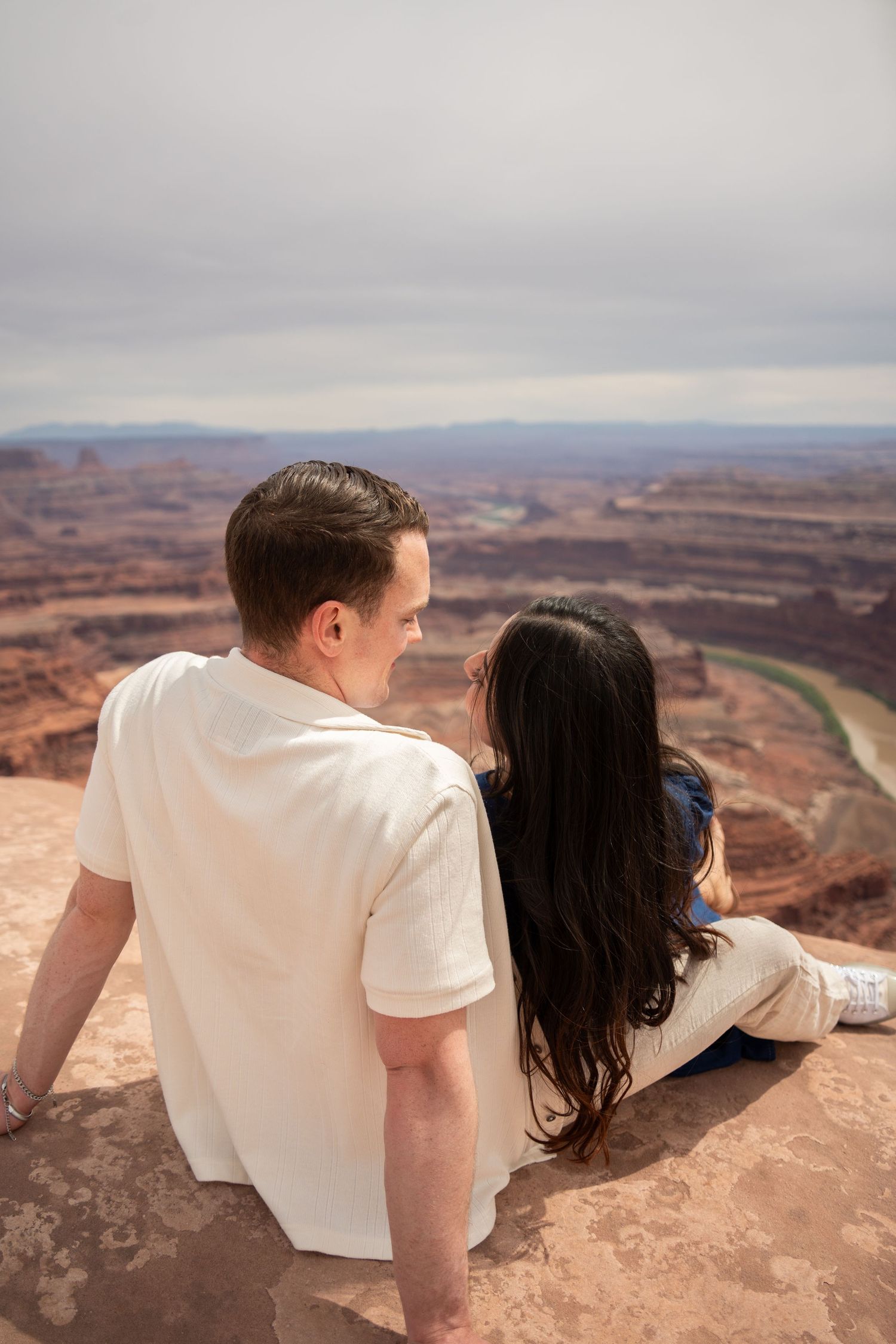 Couple sitting on canyon overlook edge enjoying scenic views at Dead Horse Point State Park