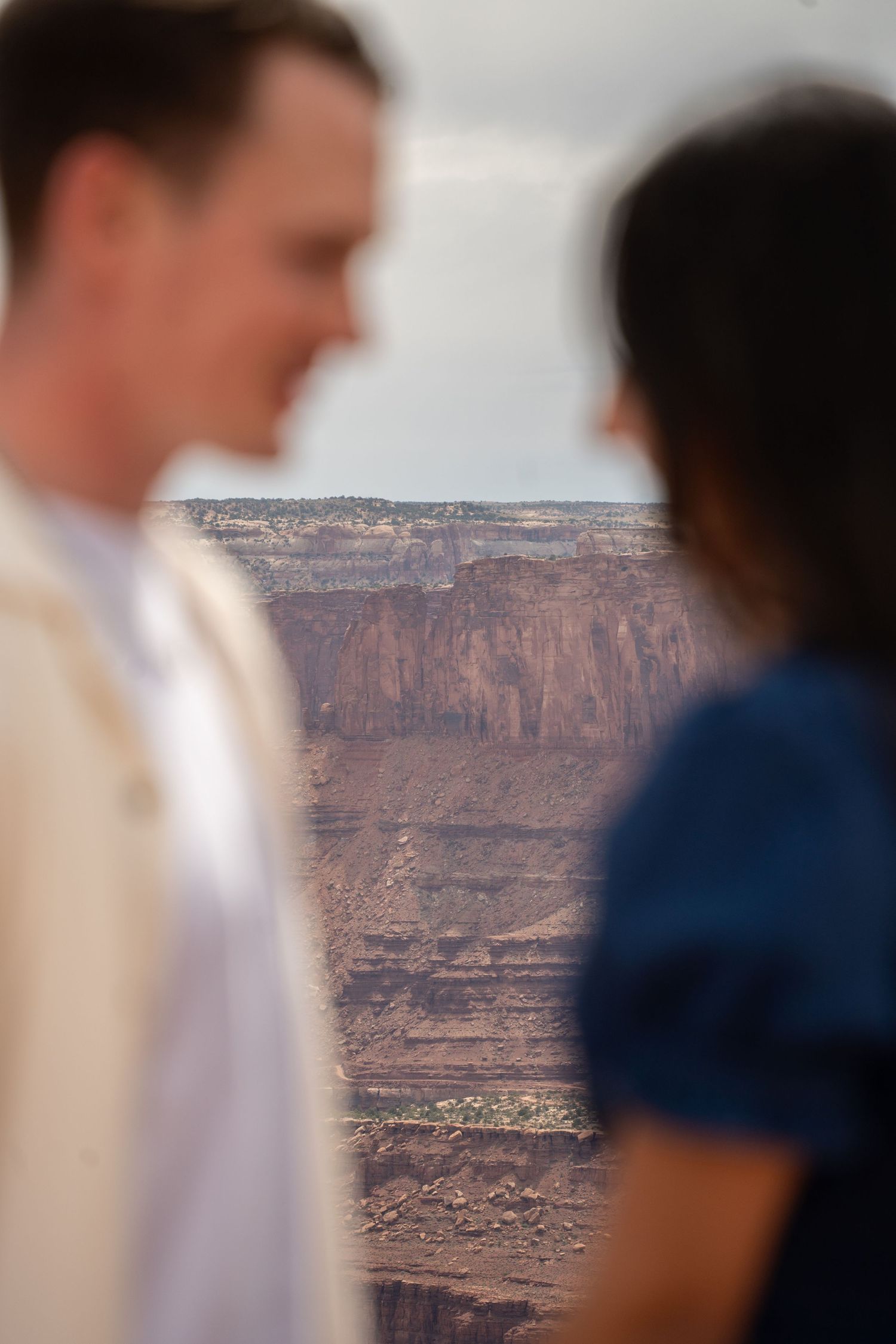 Couple standing at a canyon overlook above Canyonlands with red rock cliffs in the background