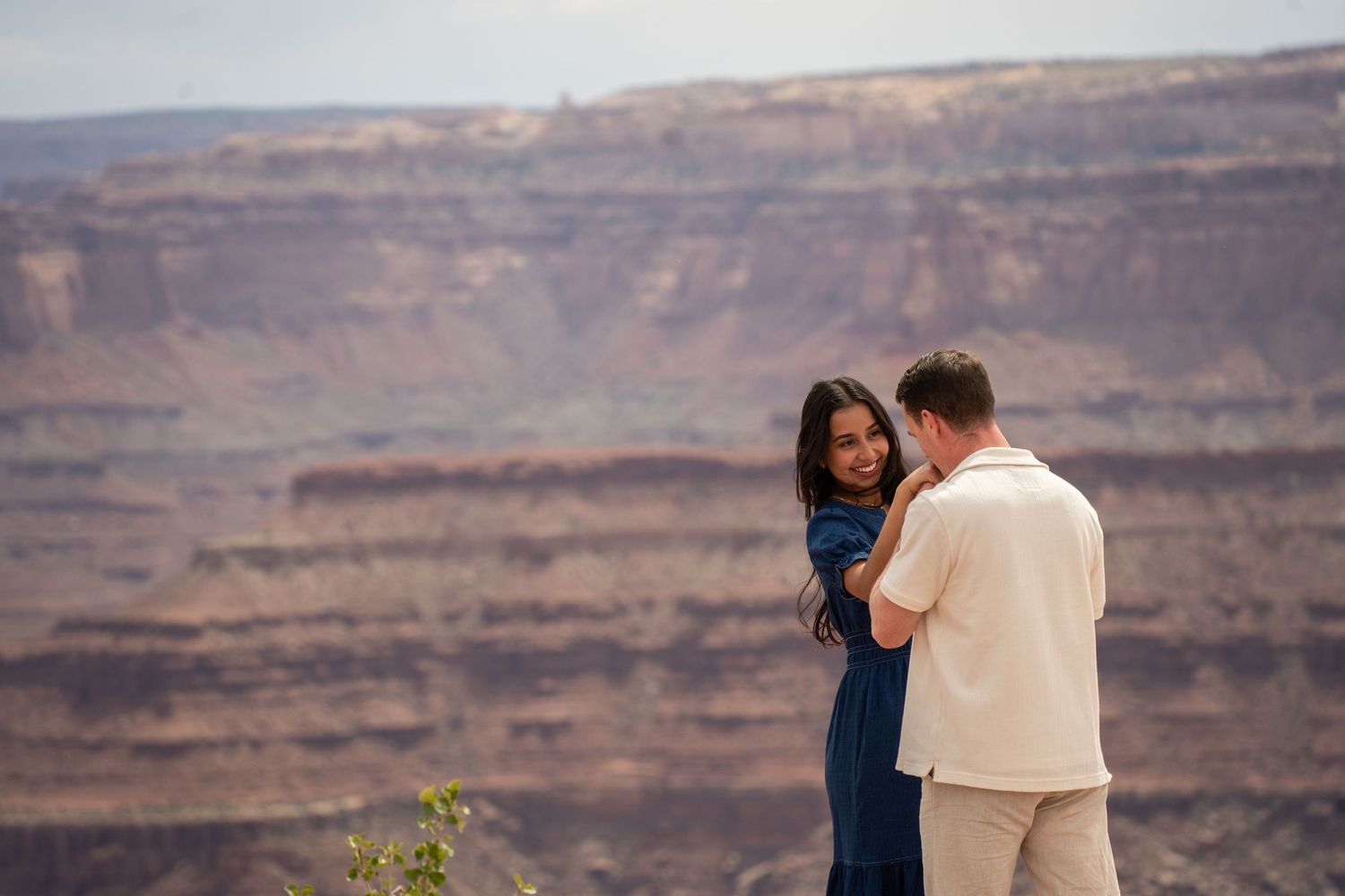 Couple sharing a romantic moment at a canyon overlook, woman in blue dress embracing man in cream shirt