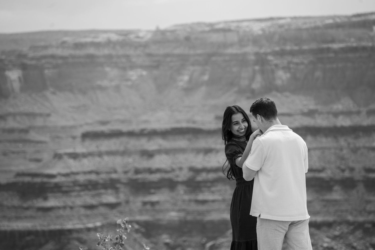 Black and white photo of a couple embracing near dead horse point canyon edge in a romantic outdoor engagement session.