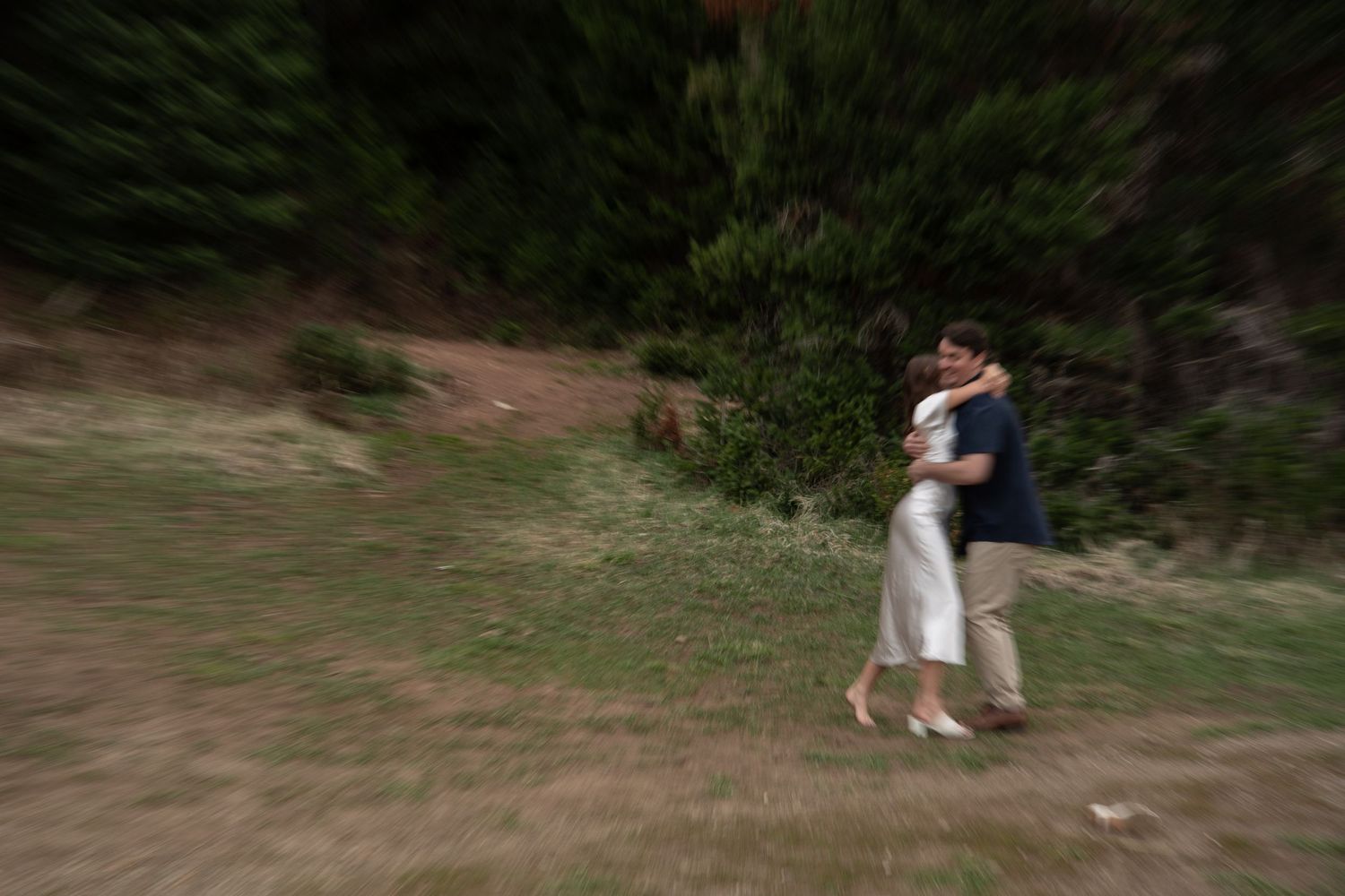 Couple embracing and dancing outdoors in a green meadow of Jordan pines with trees, captured with motion blur effect.