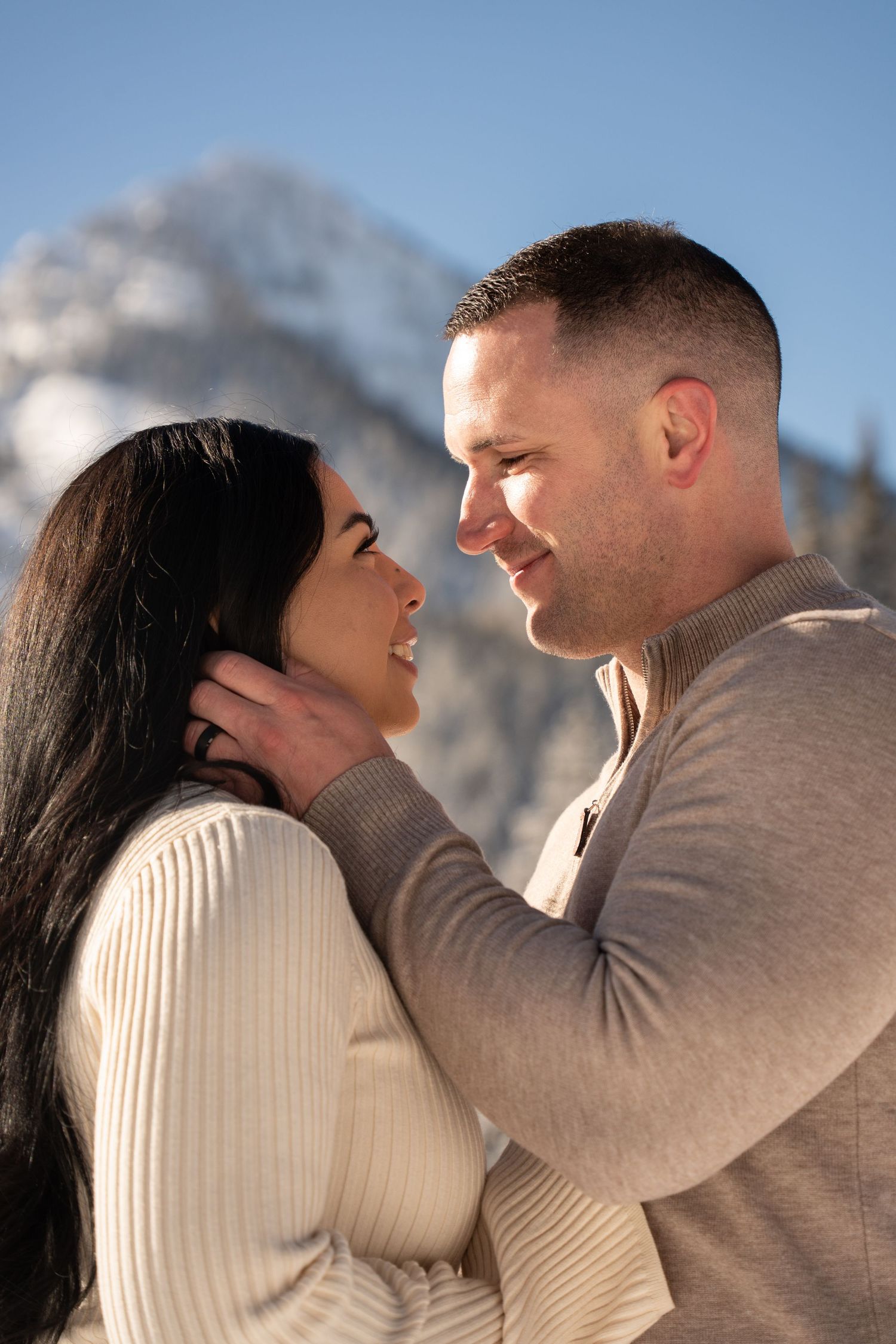 Couple sharing a romantic moment with snowy mountain backdrop in winter, wearing matching cream sweaters. tender spontaneous elopement
