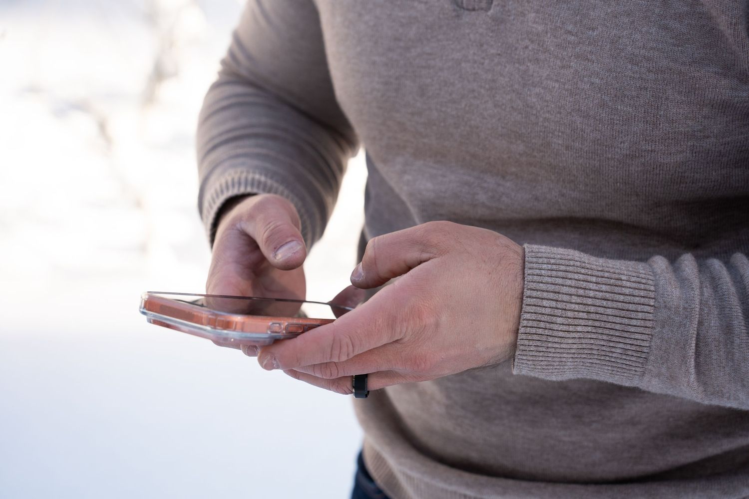 Groom in gray sweater using a smartphone to sign his marriage certificate outdoors in a bright, snowy setting.
