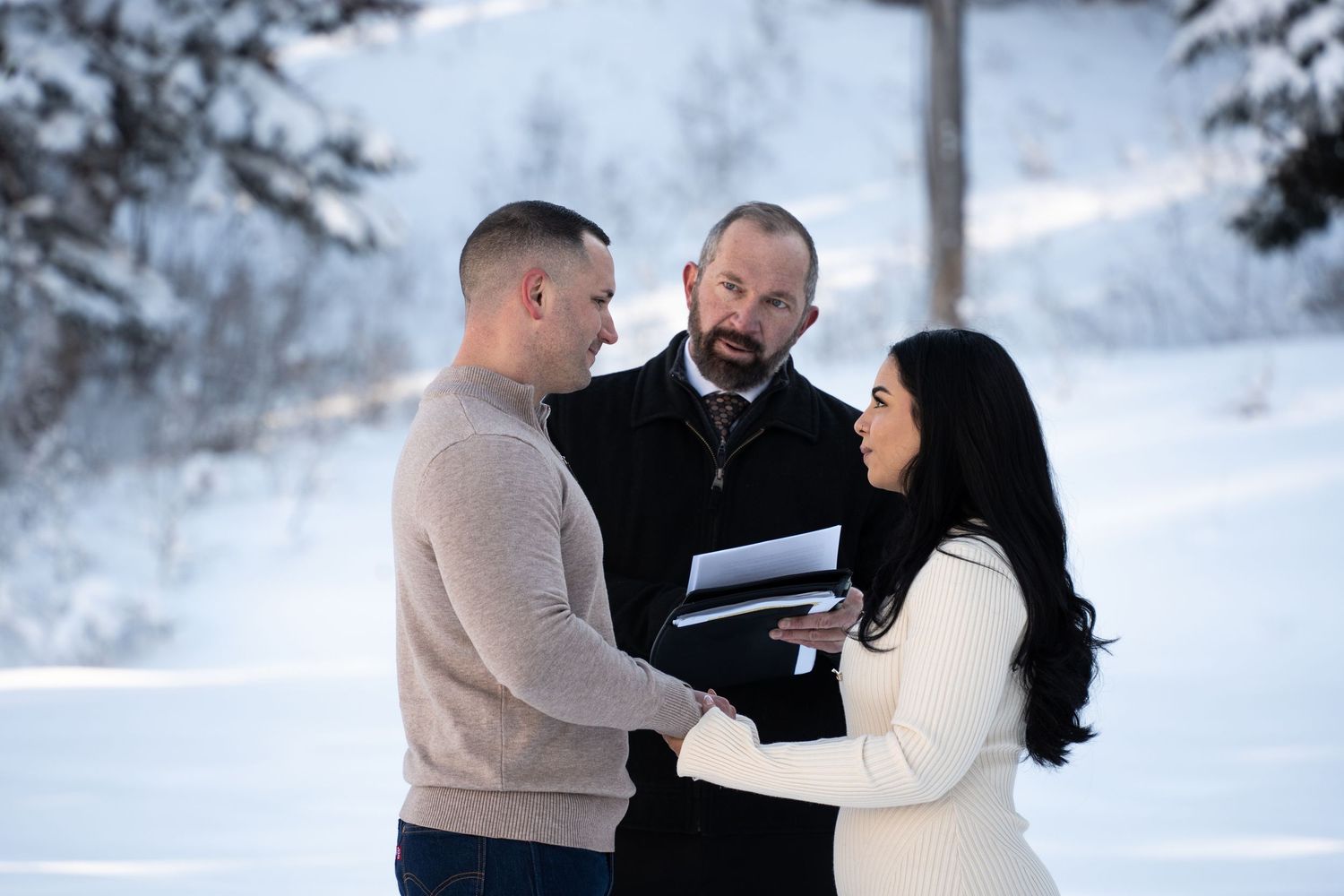 Couple exchanging vows outdoors in snowy winter landscape with officiant holding ceremony book during an intimate elopement adventure