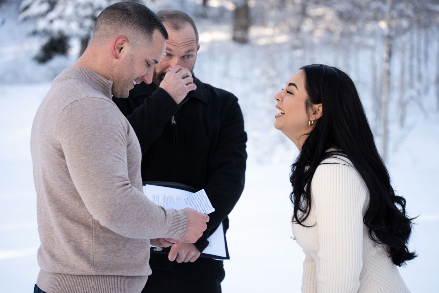 Couple exchanging vows outdoors in a snowy Wasatch mountain setting with officiant, bride smiling joyfully