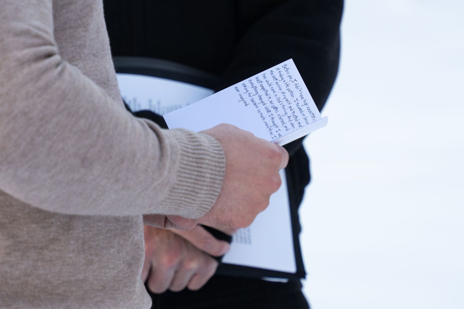 groom holding handwritten vows outdoors in snowy outdoor elopement ceremony, wearing a beige knit sweater.