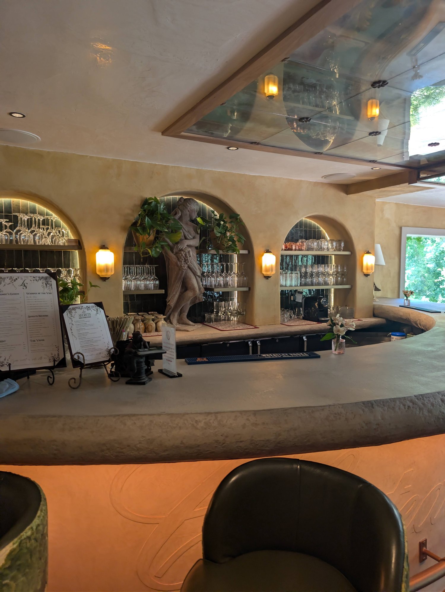 Les Secrets bar counter with a branded menu stand and stone statue among arched wall nooks