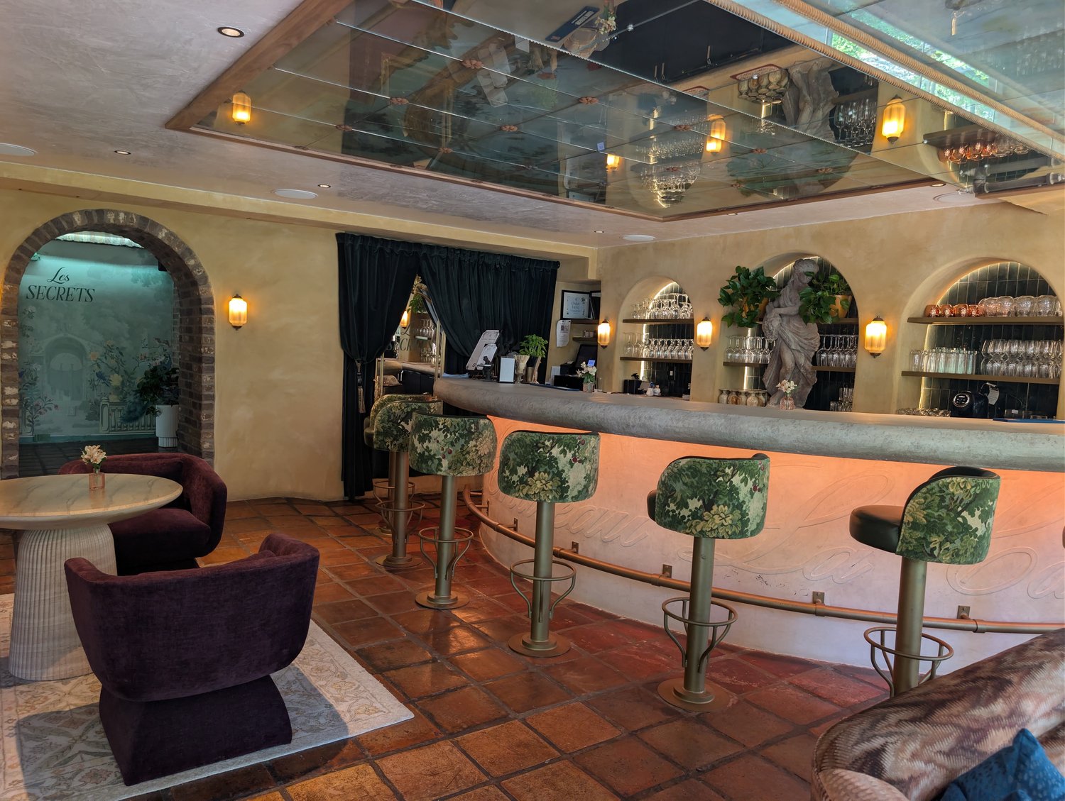 Les Secrets sign above floral-patterned bar stools and purple velvet lounge chairs