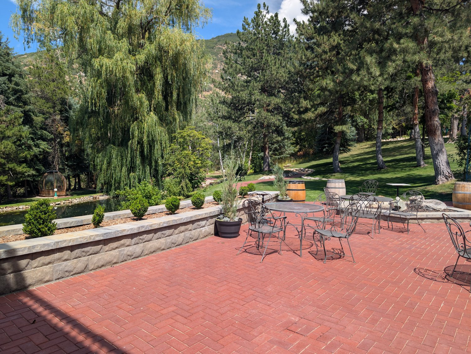 La Caille's outdoor restaurant deck with wrought-iron cafe tables, a weeping willow, and a pond