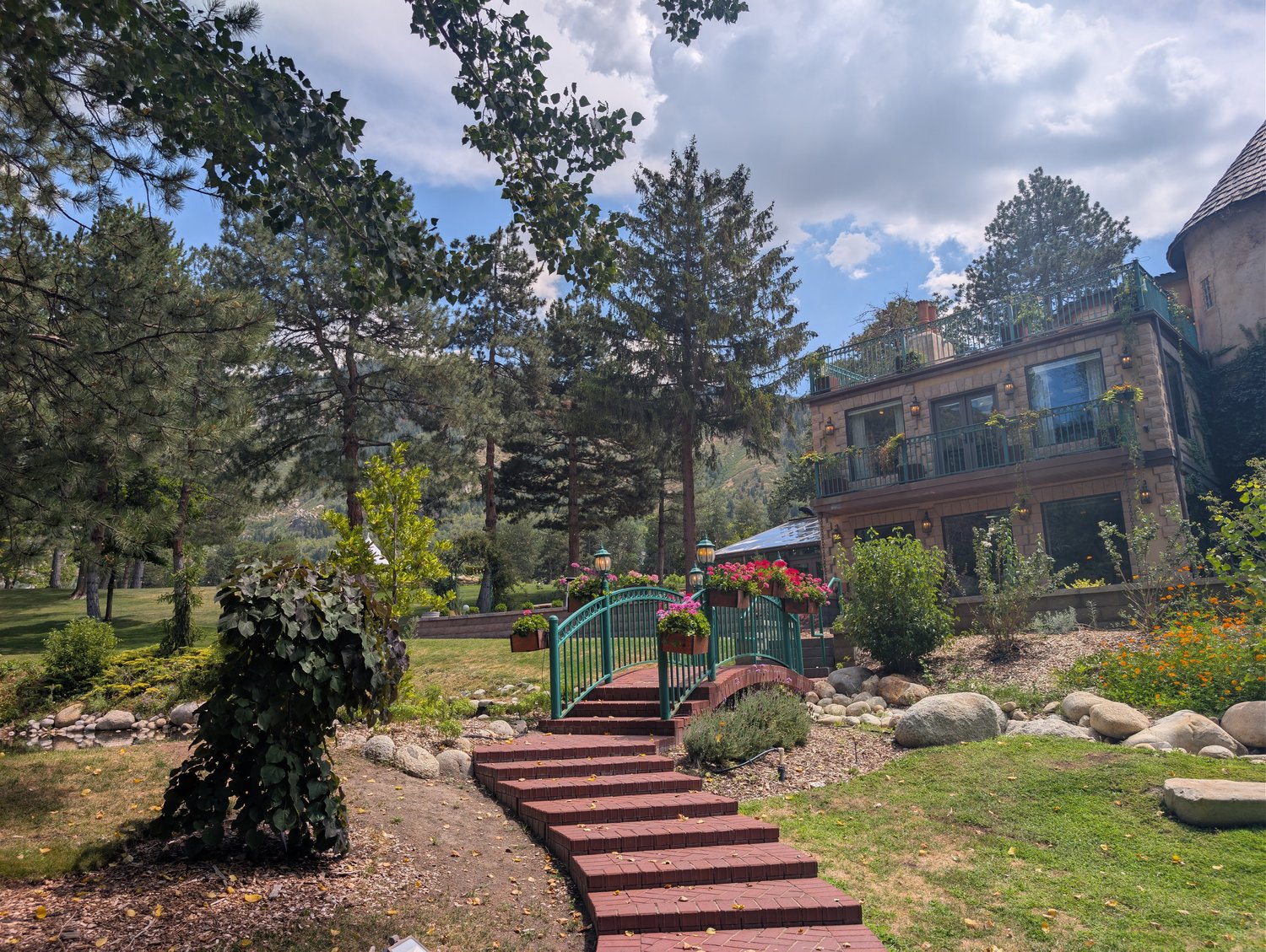 Brick steps and an arched footbridge leading toward La Caille's main building, with mountains behind