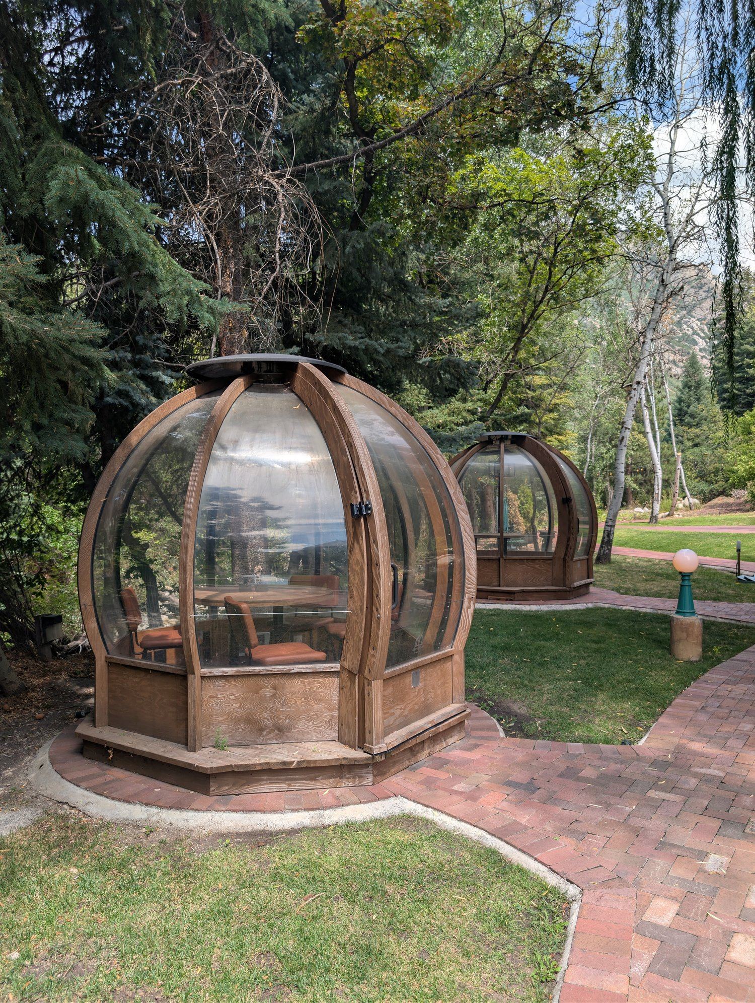 Glass-domed wooden Alpine Pods with a table and chairs inside, set among the trees at La Caille