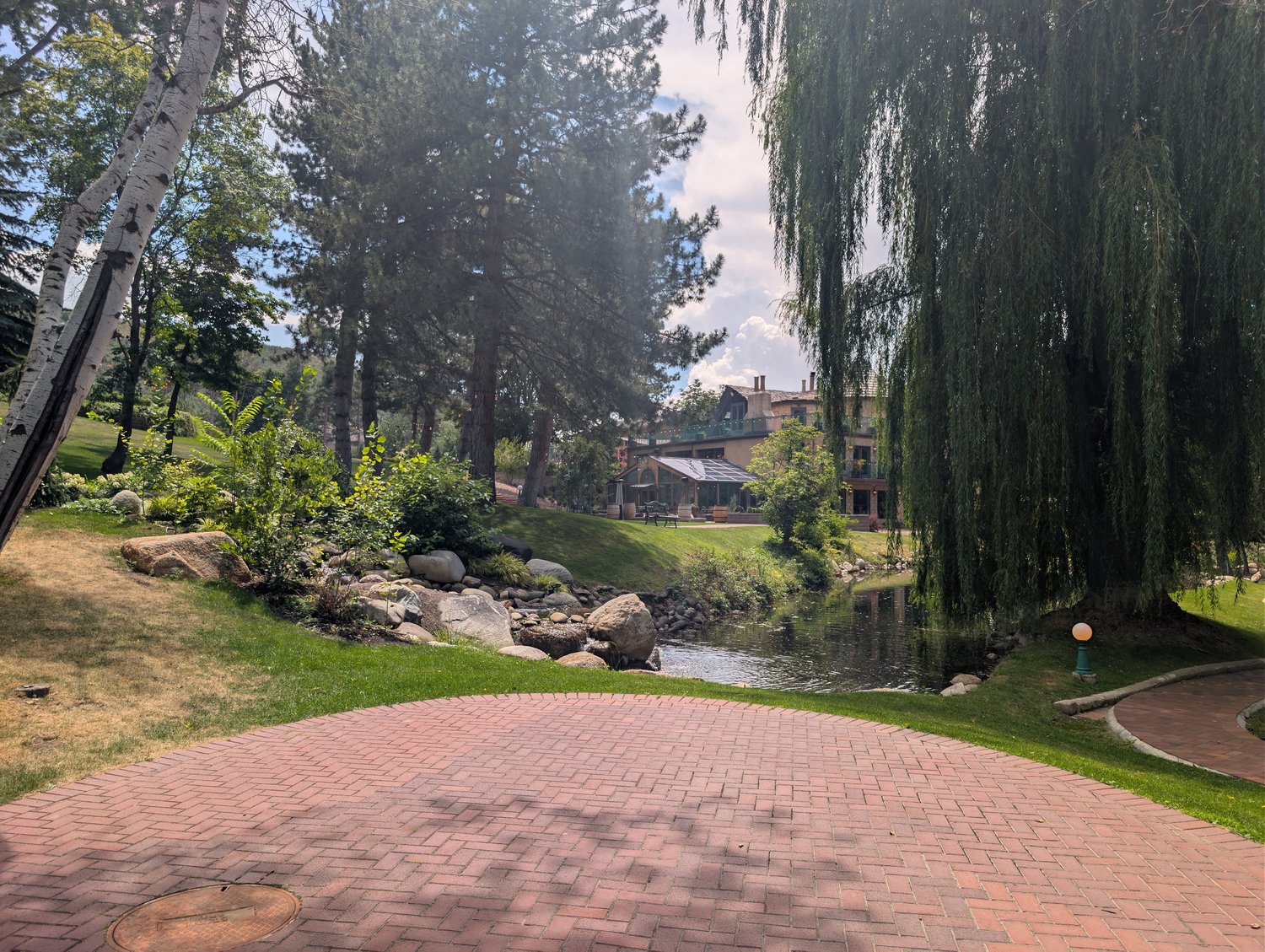 Brick patio beside a stream and weeping willow at La Caille, with a view back toward the restaurant