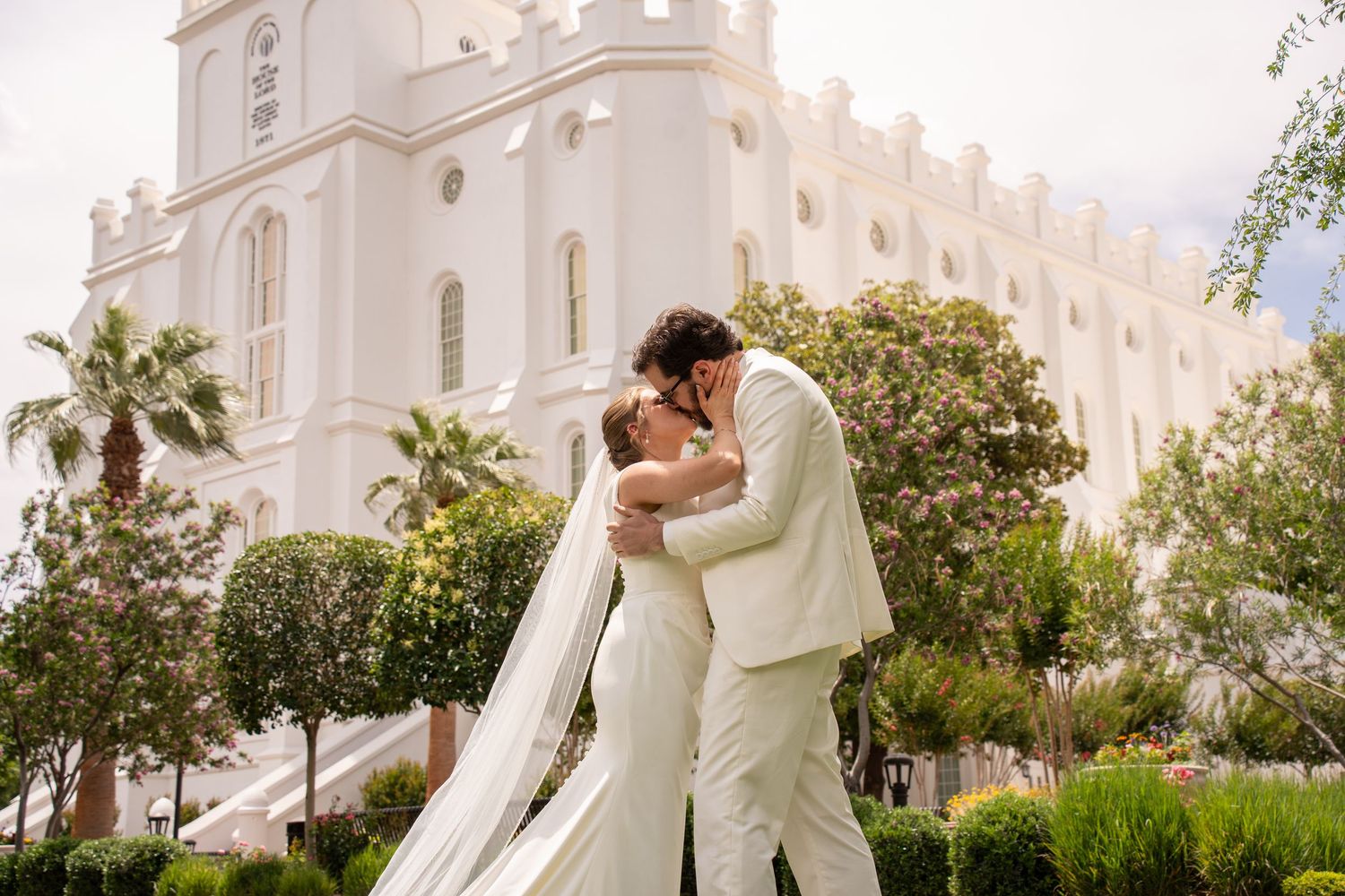 Bride and groom share a romantic kiss outside saint george lds temple surrounded by palm trees on their wedding day.