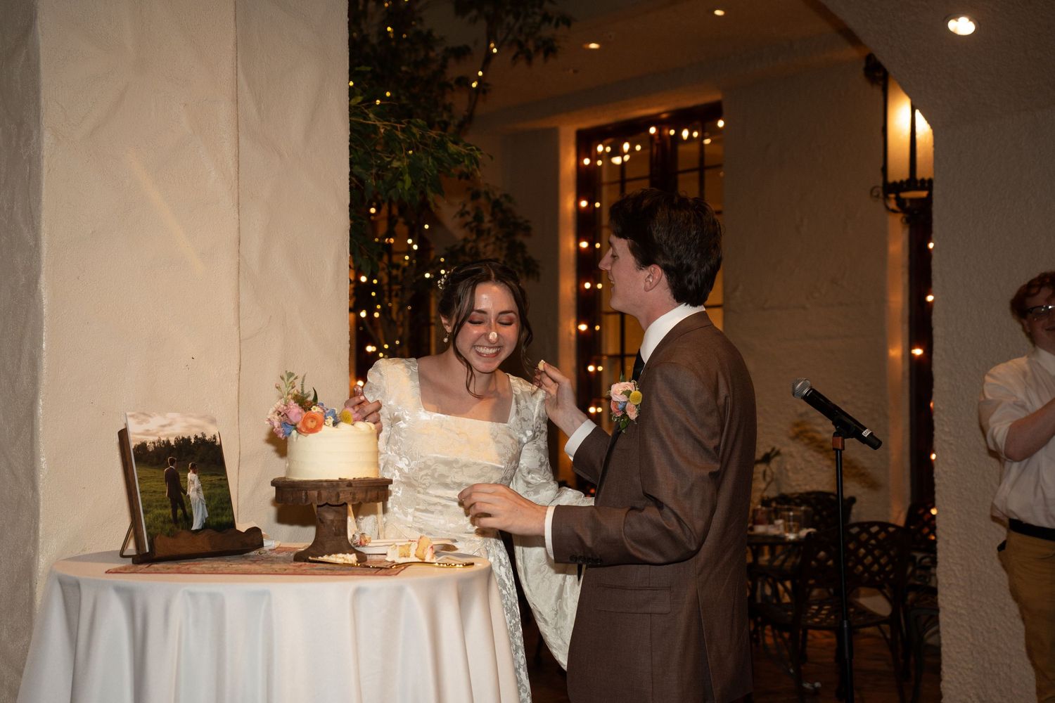 Bride and groom laughingly cutting their wedding cake together at in Springville Museum of Art with warm string lights.