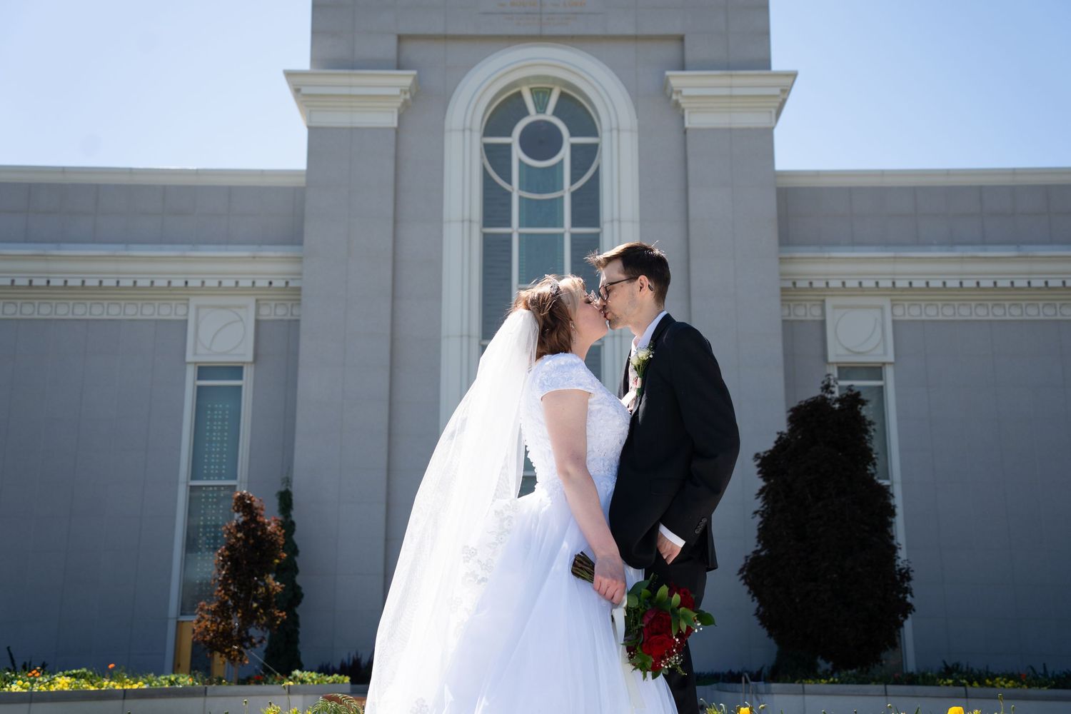 Bride and groom share a romantic moment outside Mount Timpanogos LDS Temple on a sunny day.