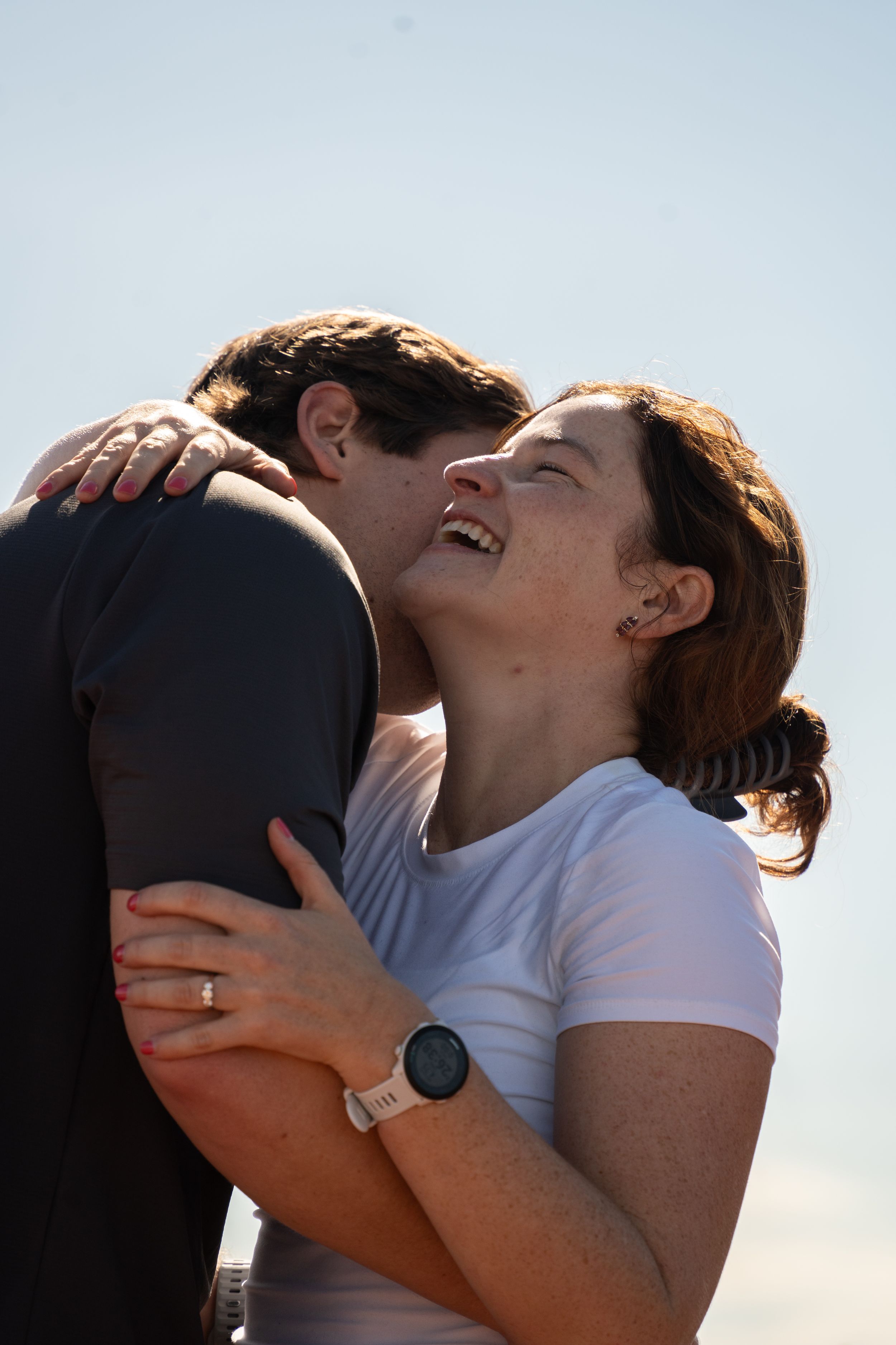 Man kneeling to propose to woman on a mountain ridge with the valley spread out behind him