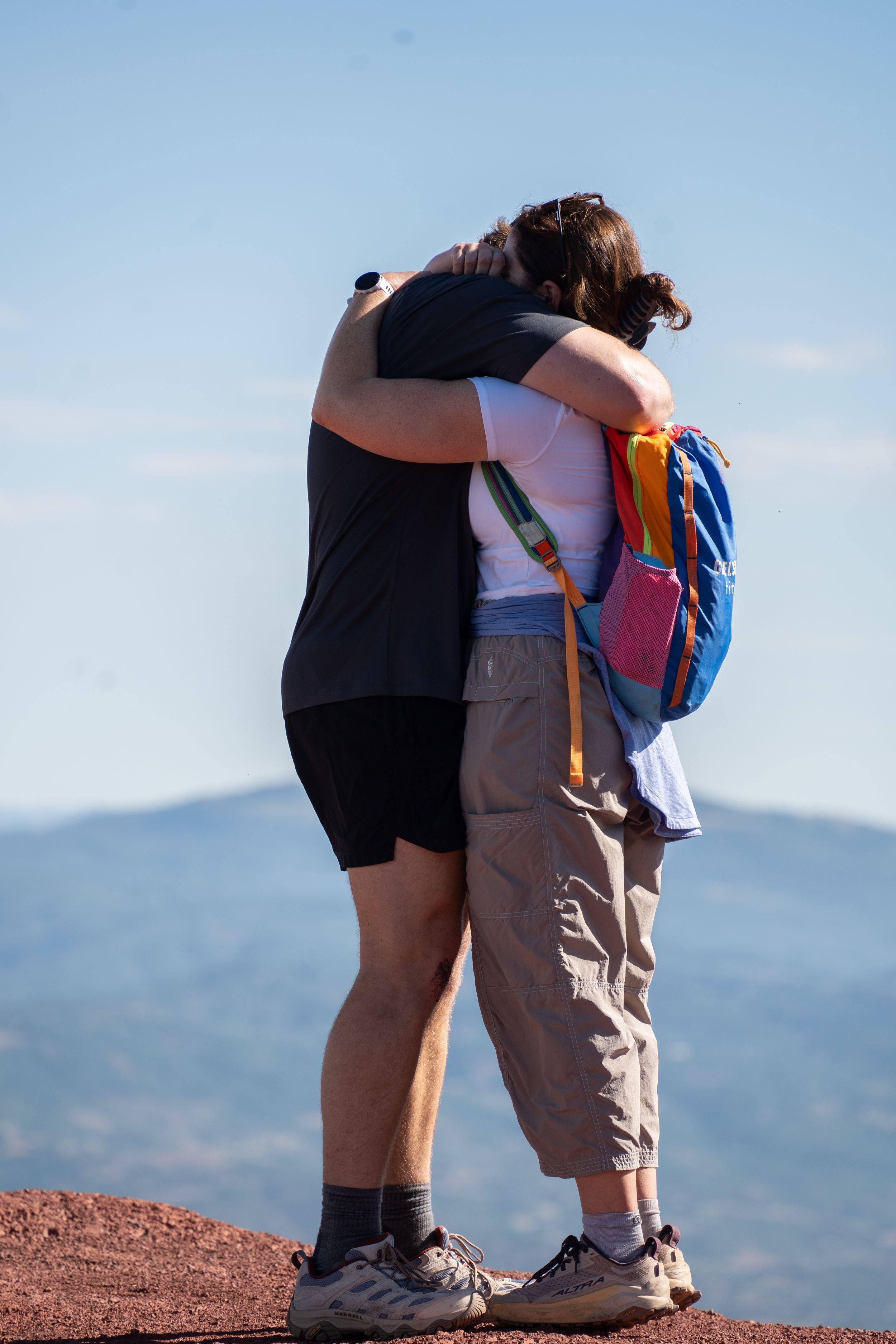 Couple embracing at a mountain overlook with a wide valley view behind them