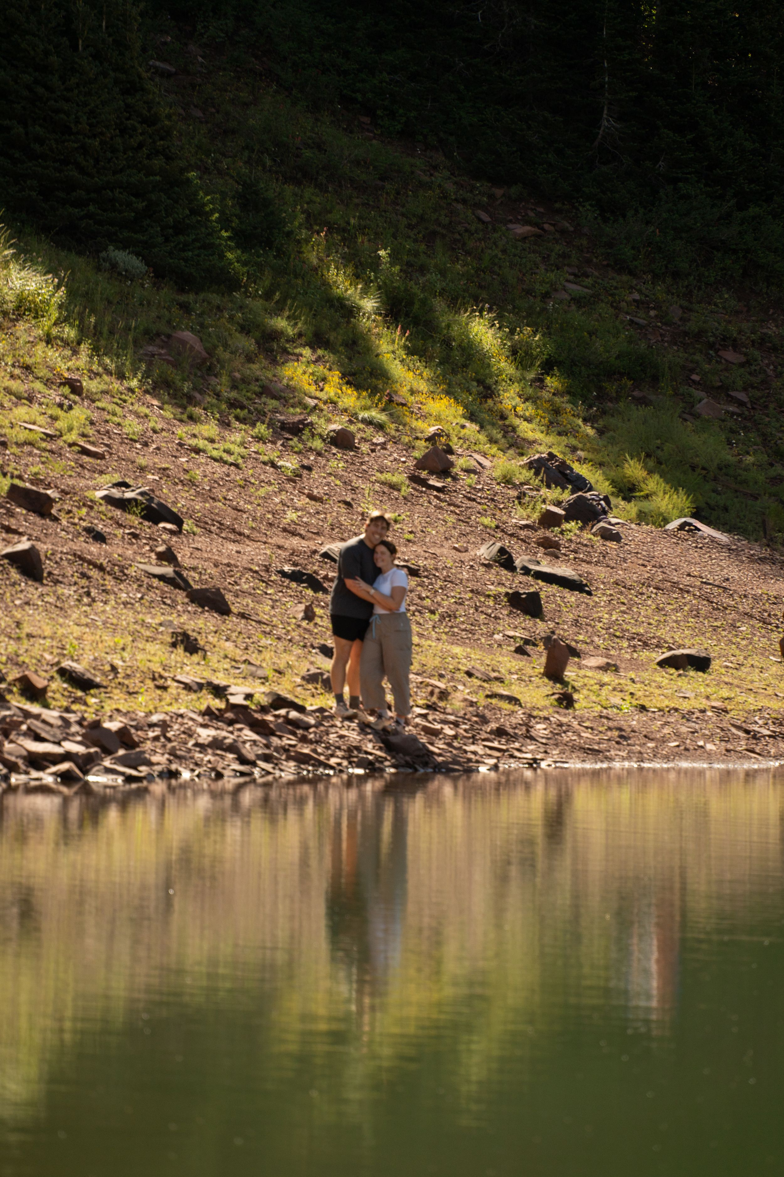 Couple standing at the edge of a mountain lake with their reflection in the still water
