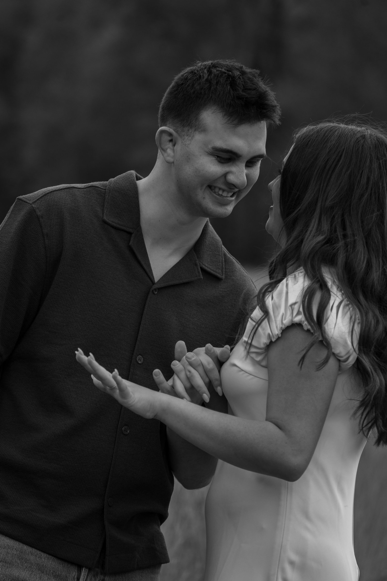 Close-up black and white photo of a newly engaged couple laughing together moments after a surprise proposal