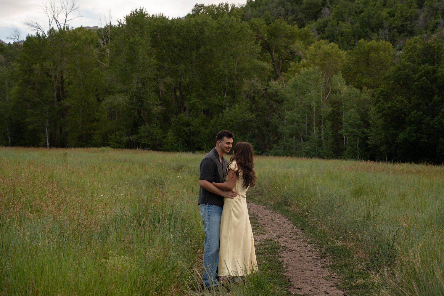 Newly engaged couple embracing on a dirt trail surrounded by tall grass in Provo Canyon