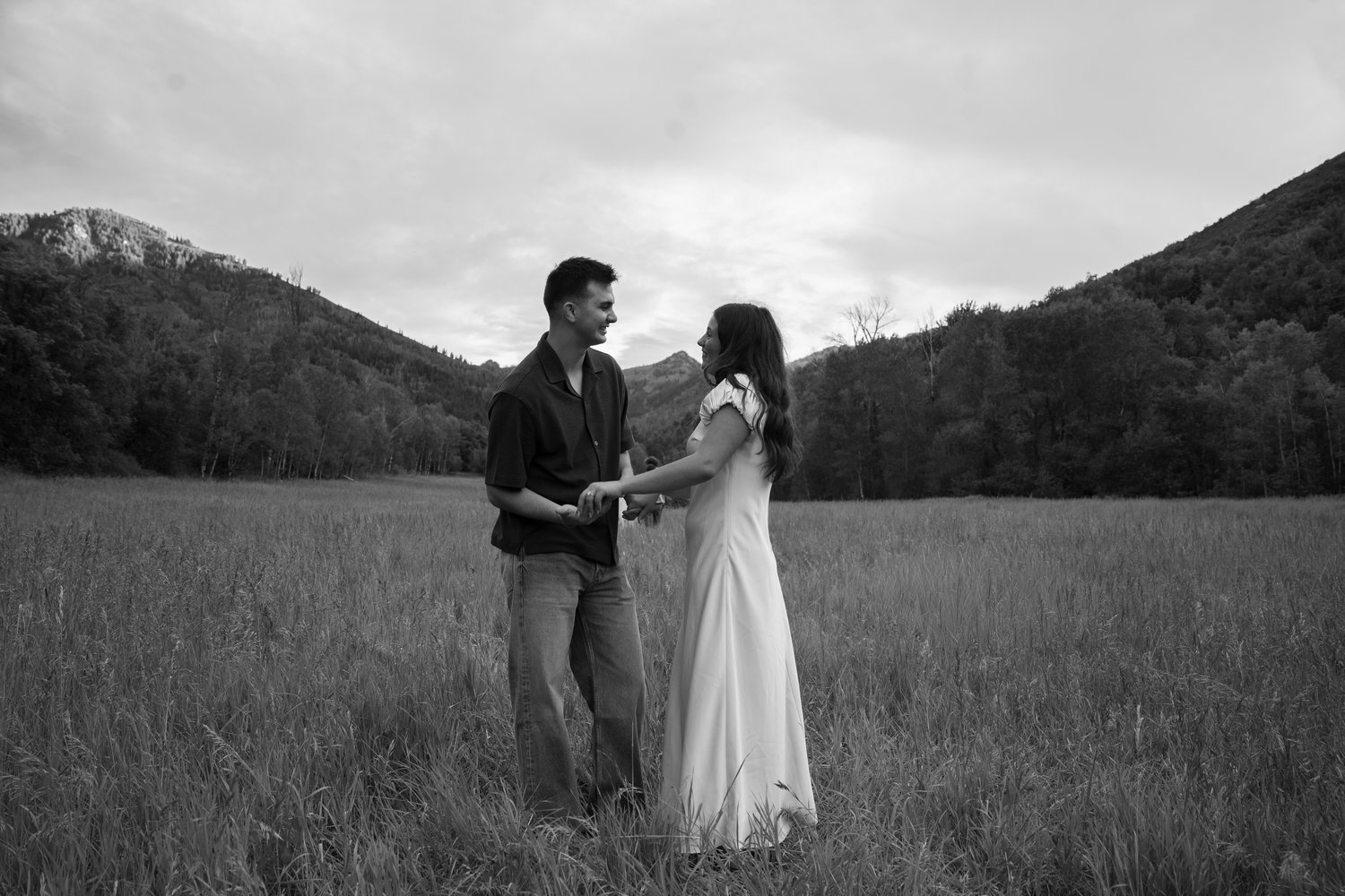 Black and white photo of a couple facing each other and holding hands in an open mountain meadow