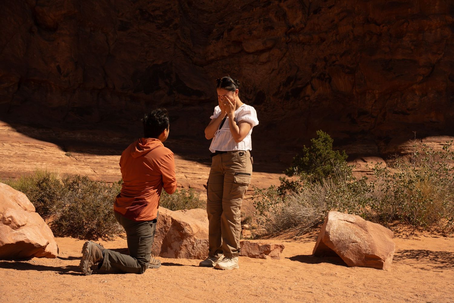 Person kneeling proposing to partner at scenic red rock canyon desert landscape with sandstone boulders.
