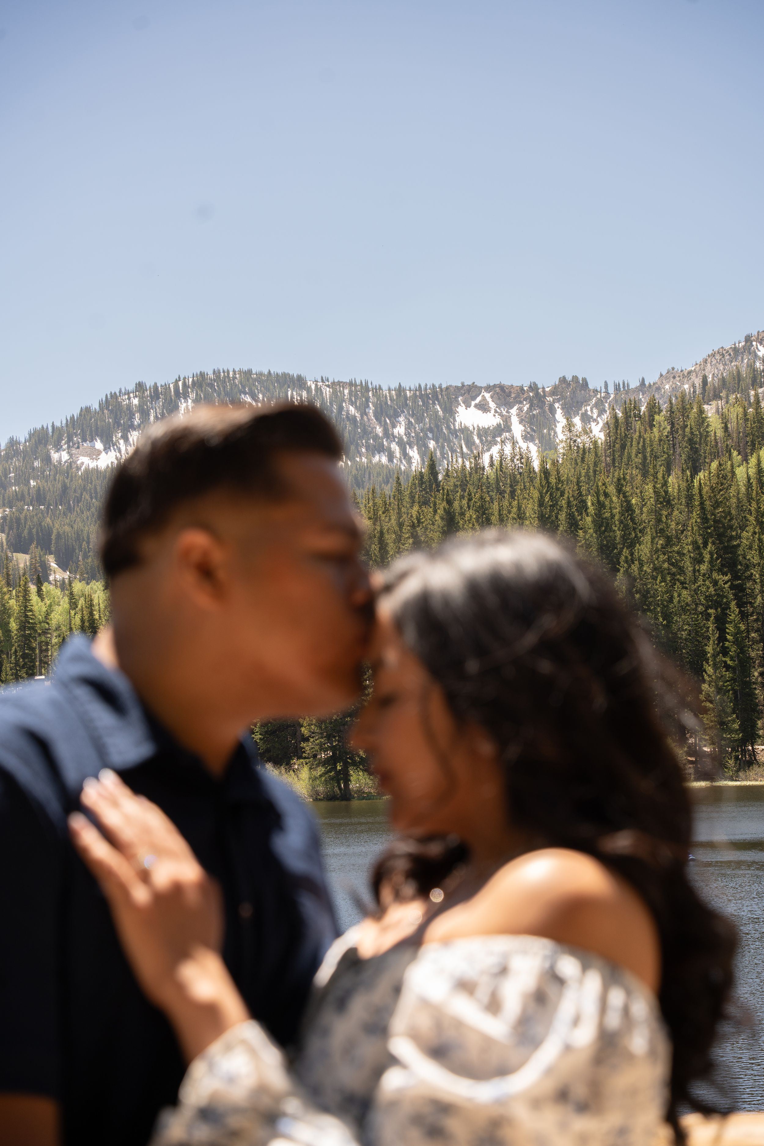 Couple sharing a romantic kiss with a silver lake and snow-capped peaks in the background.