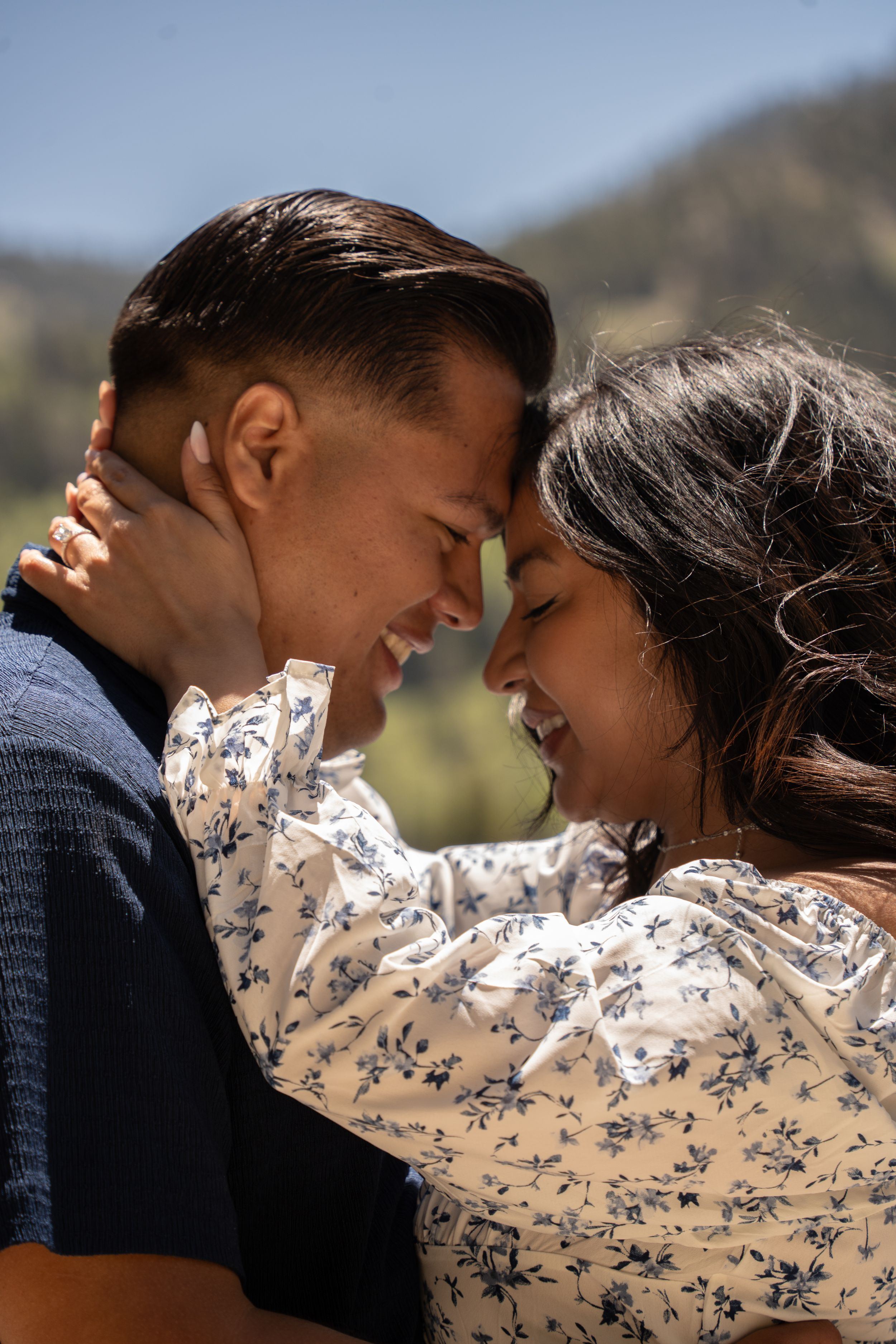An engaged couple smiles and touches foreheads in a romantic outdoor embrace with uinta mountains and big cottonwood canyon