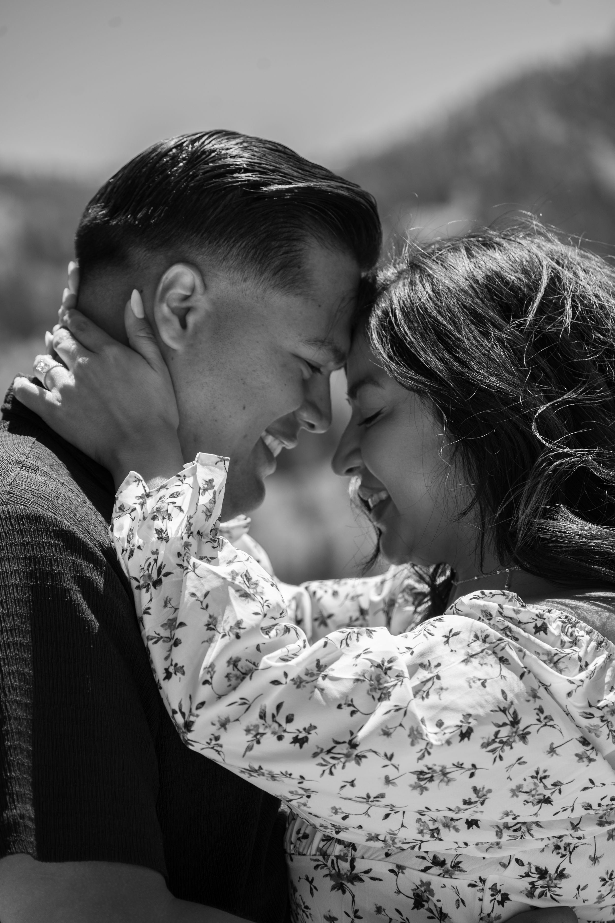 Black and white photo of a couple embracing outdoors, smiling and touching foreheads in a romantic moment in big cottonwood canyon