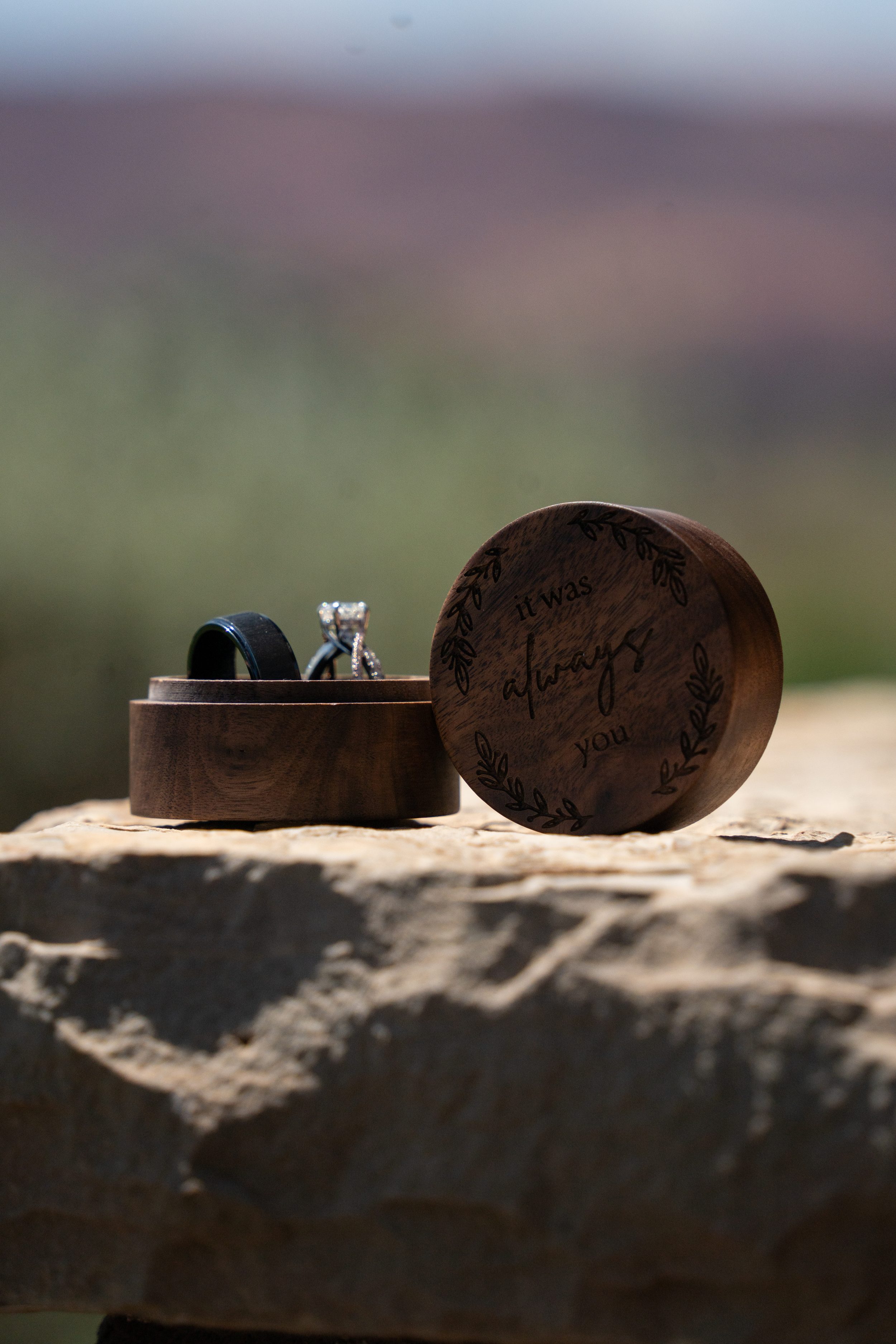 Wooden ring box engraved with 'it was always you' holding the wedding rings, resting on red rock at Pioneer Park.
