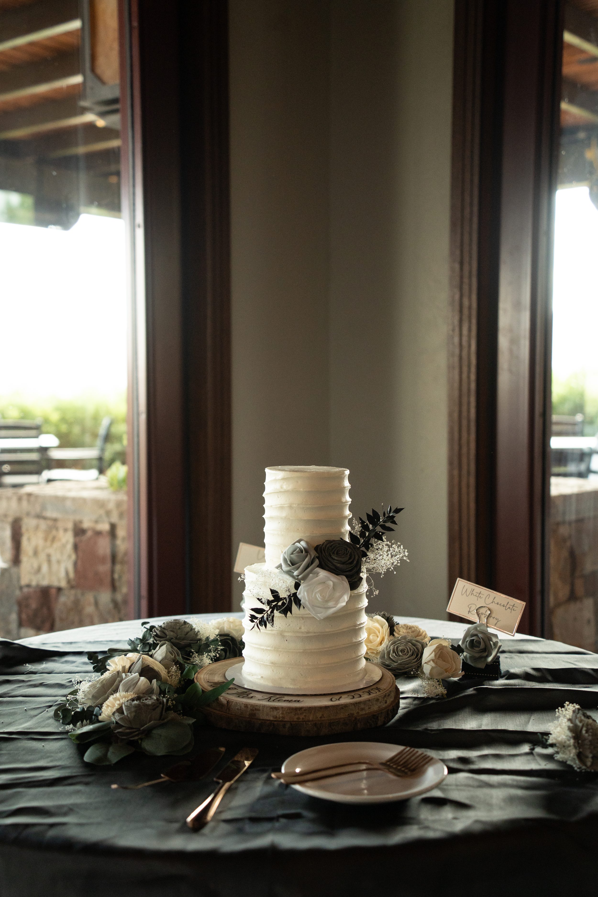Two-tier white wedding cake with black and gray sola wood roses on a personalized wood cake stand.