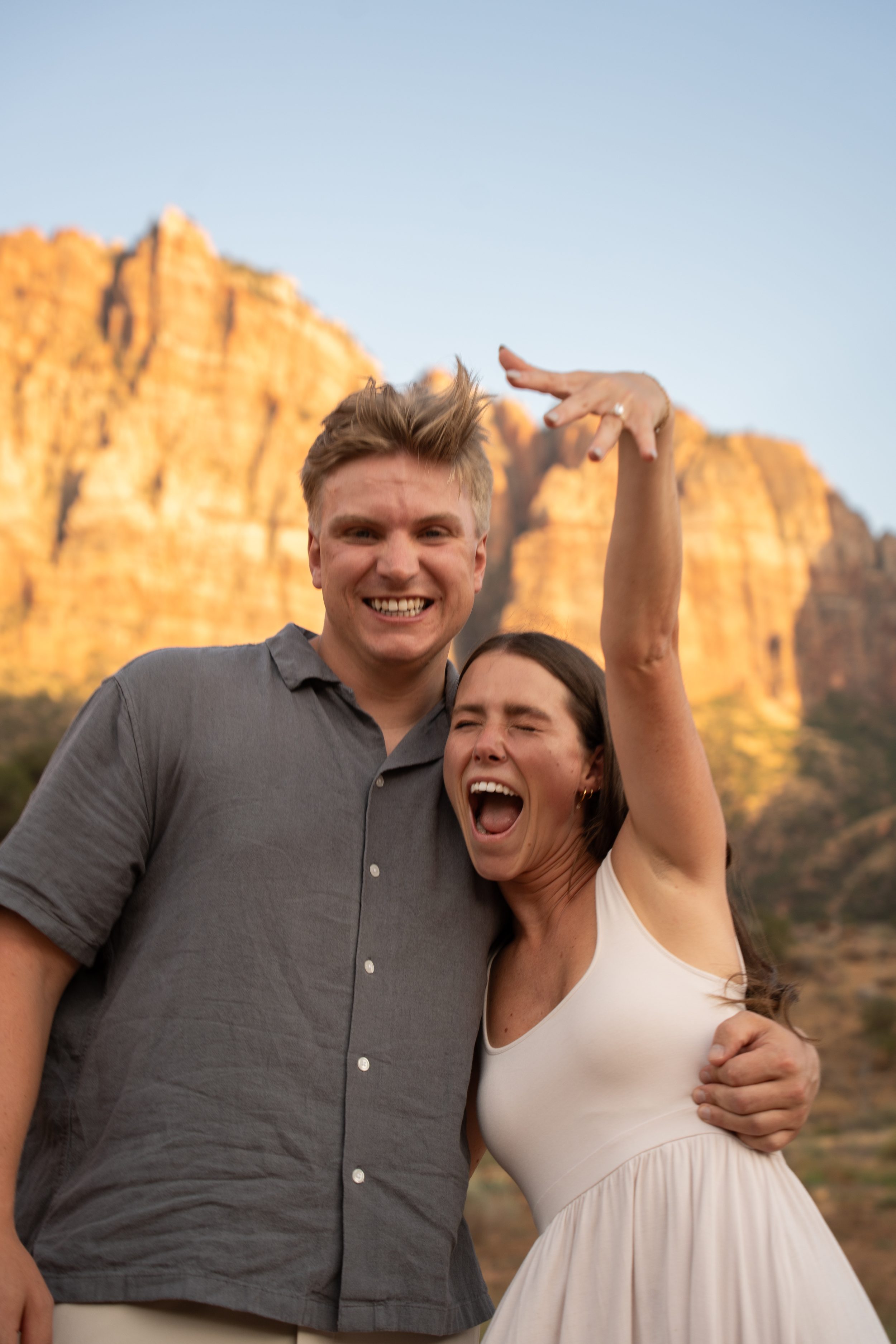 Lyndsey laughing and raising her hand to show off her new ring next to a smiling Jack.
