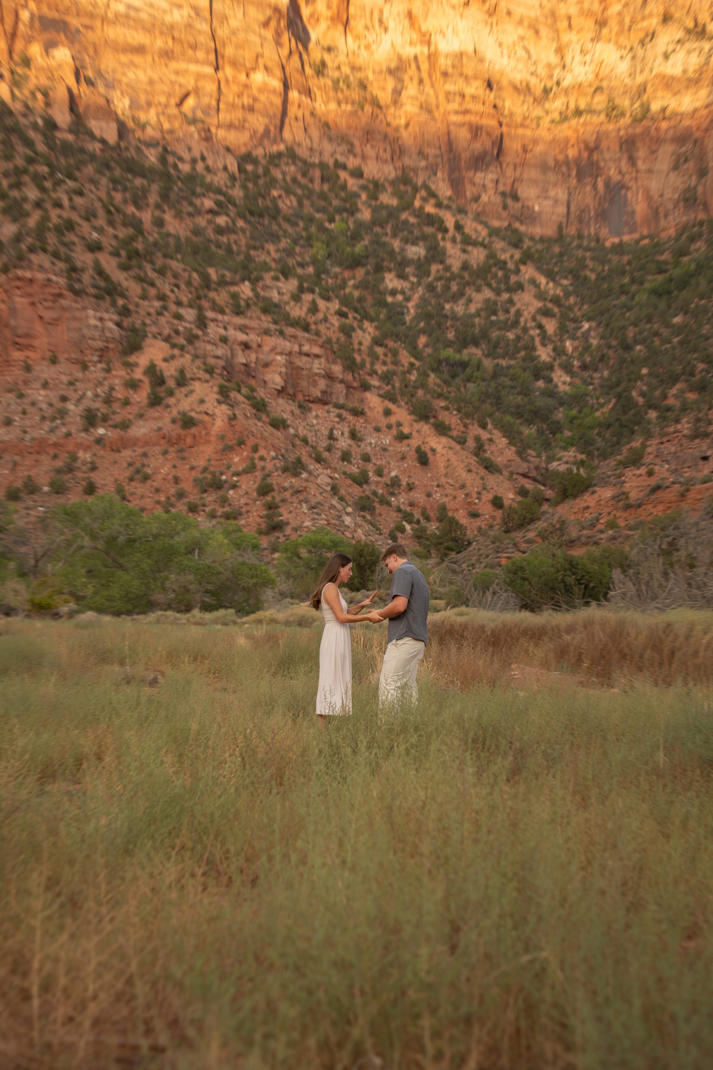 Jack and Lyndsey walking hand in hand through the meadow, laughing, with the canyon wall behind them.