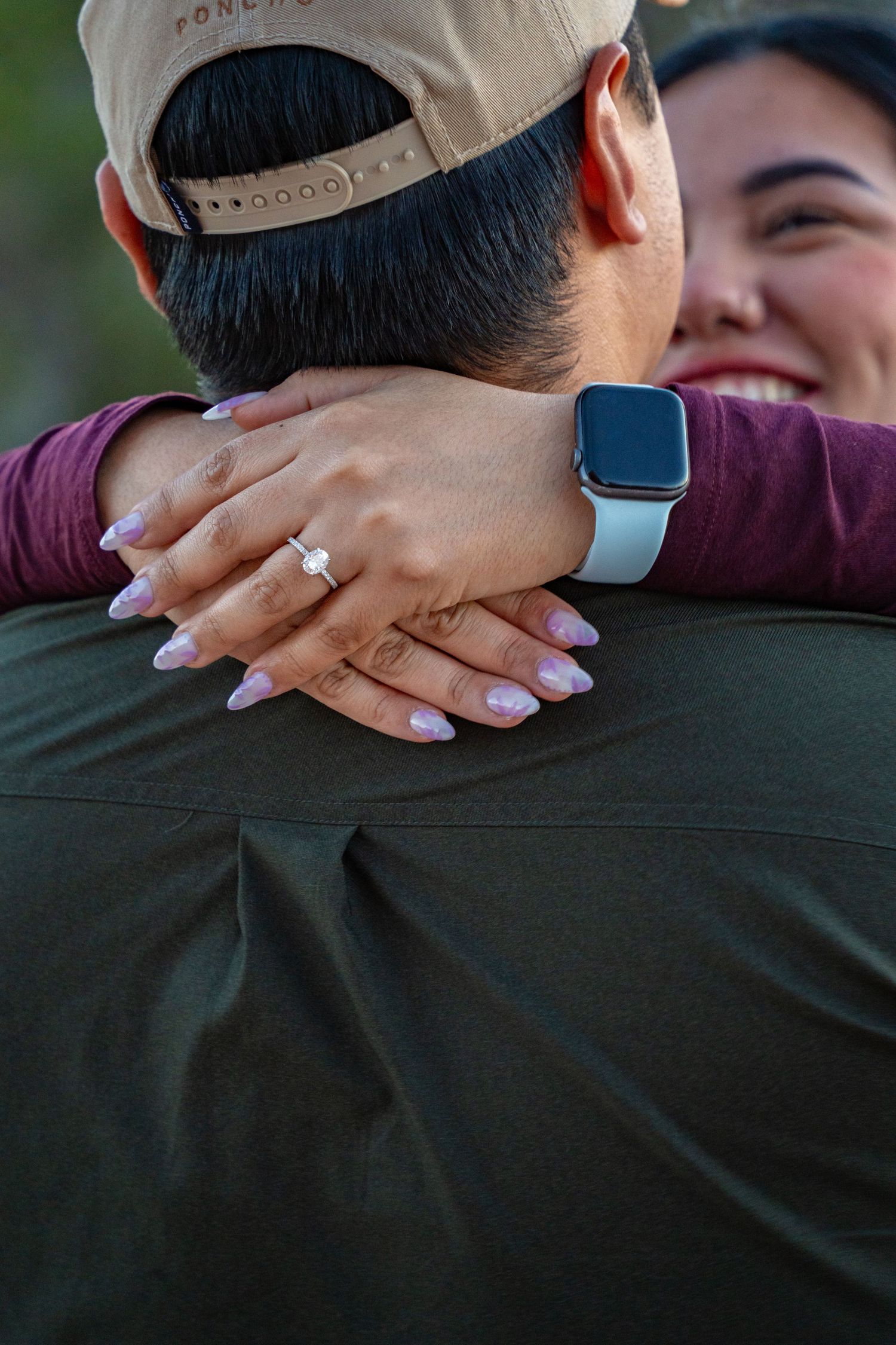 Couple embracing after engagement, woman showing diamond ring and smartwatch, smiling joyfully facing her fiance