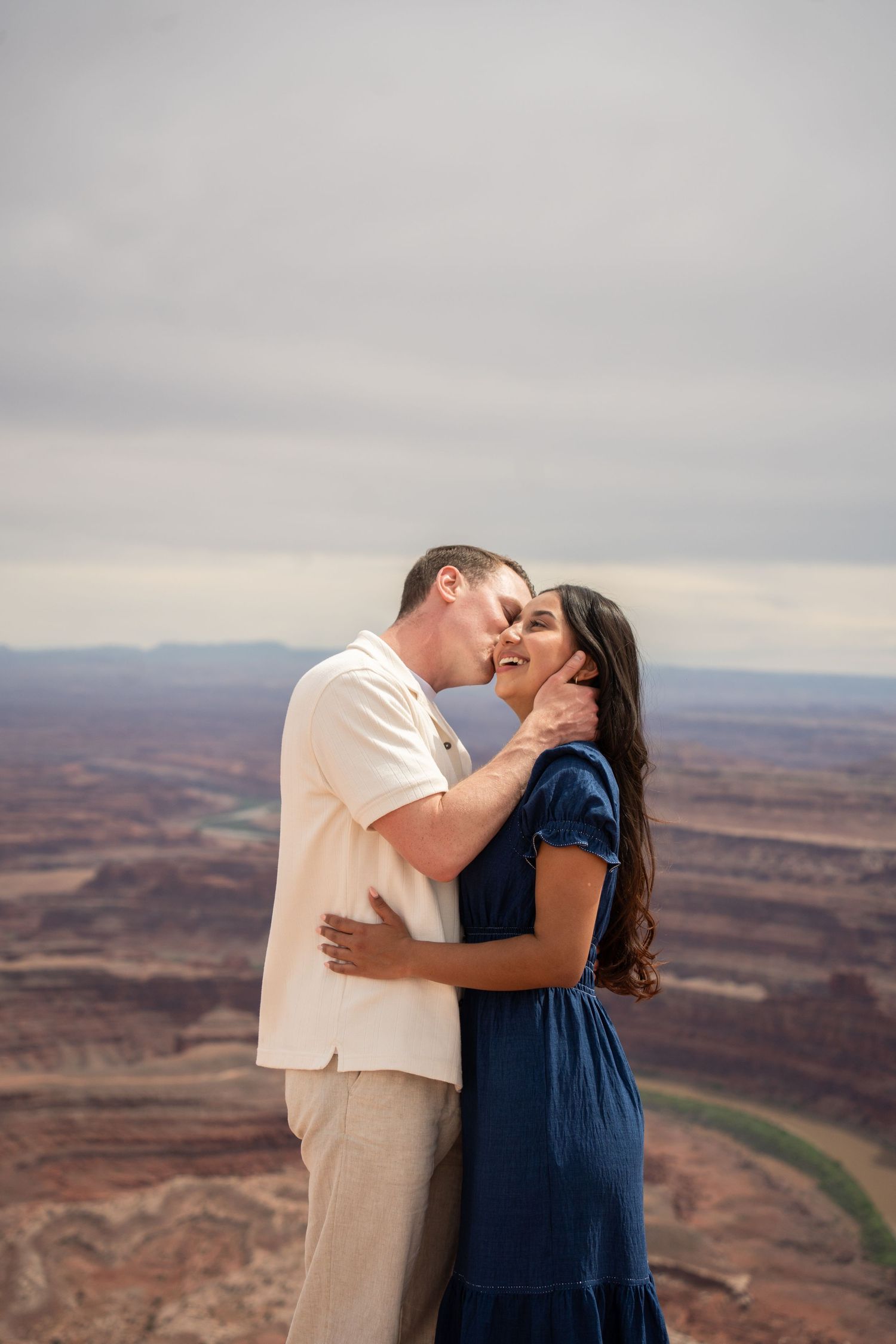 Couple sharing a romantic kiss at Dead Horse Point overlook with stunning red canyon landscape backdrop.