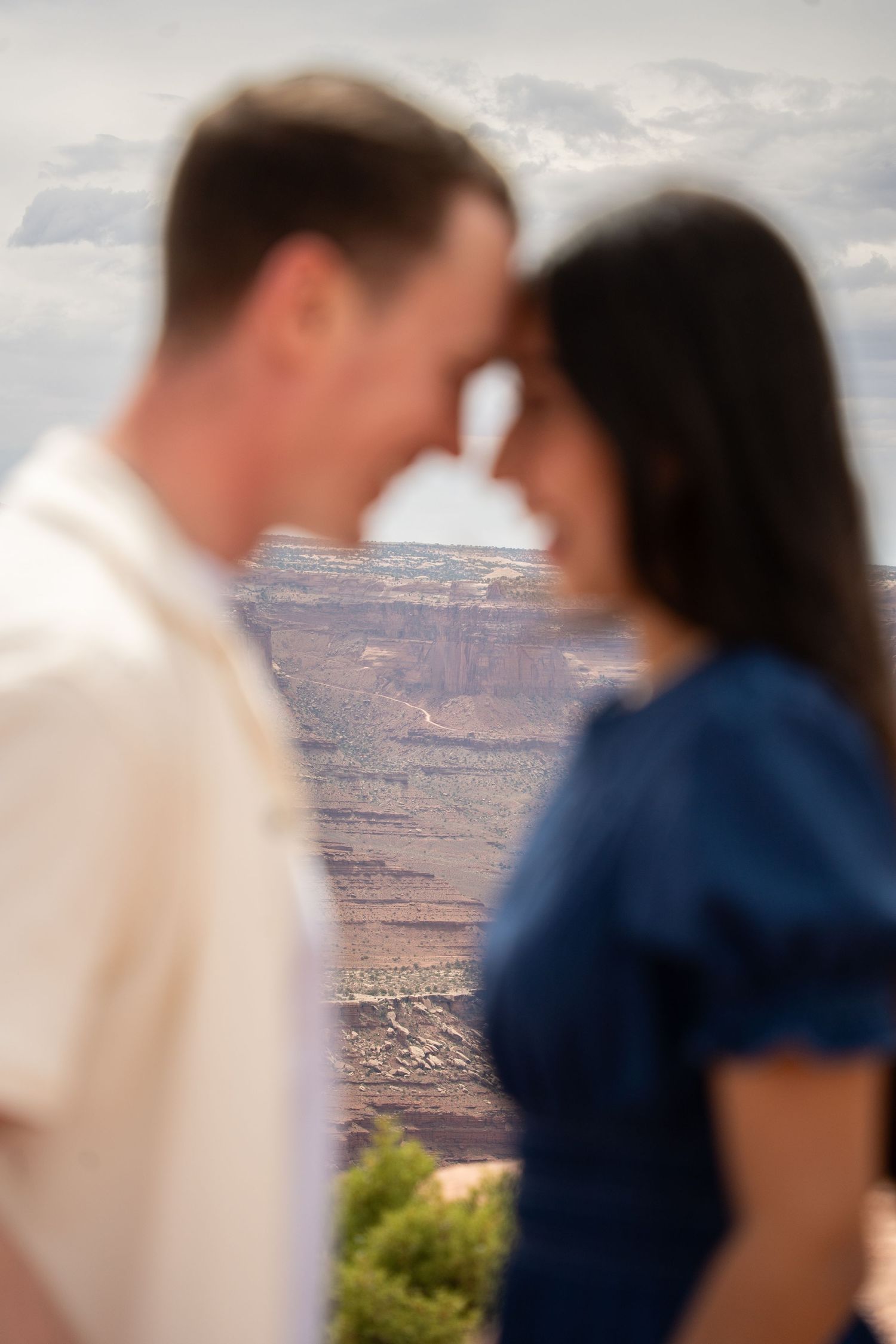 Blurred couple sharing romantic moment with stunning canyonlands landscape and cloudy sky in background.
