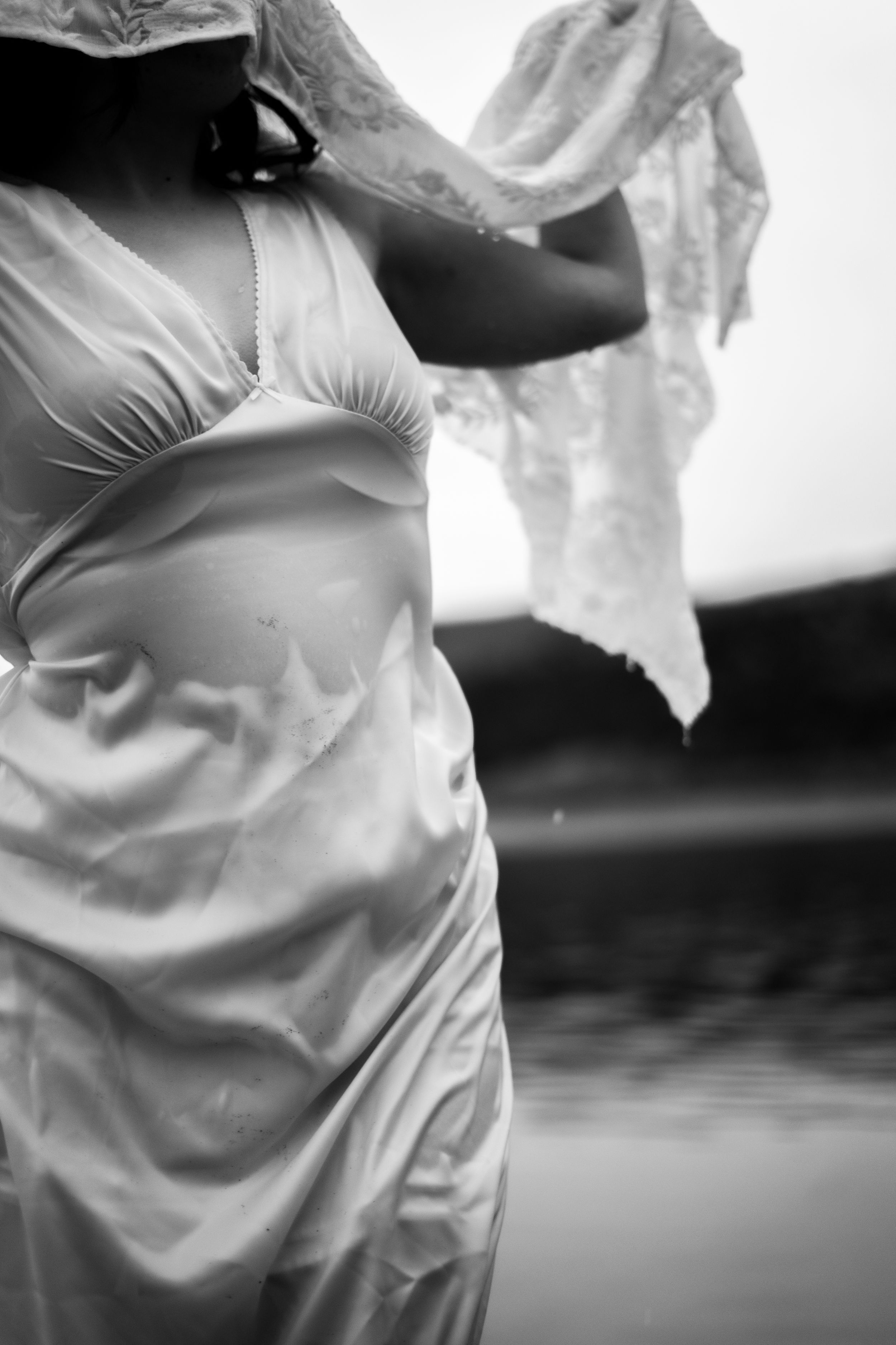 Black and white photo of a woman in a wet satin dress holding lace fabric outdoors during boudoir outdoor photoshoot.