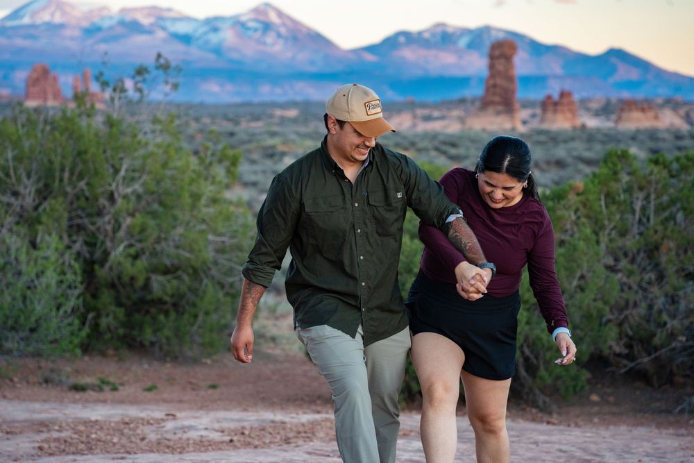 Couple holding hands and laughing while walking on a Moab desert trail