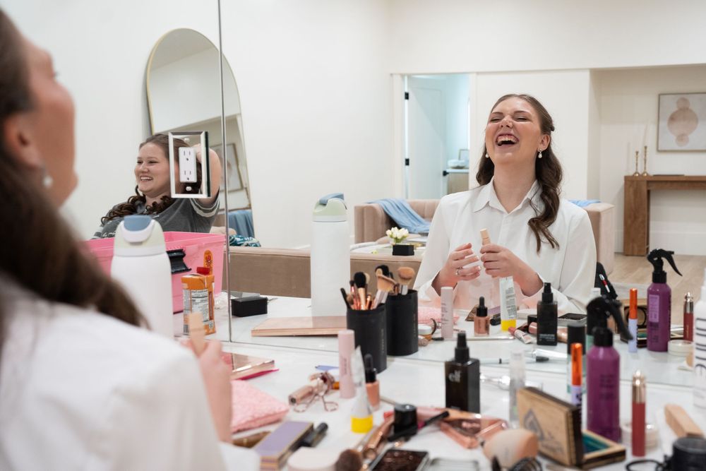 Bride laughing at makeup vanity mirror surrounded by beauty products