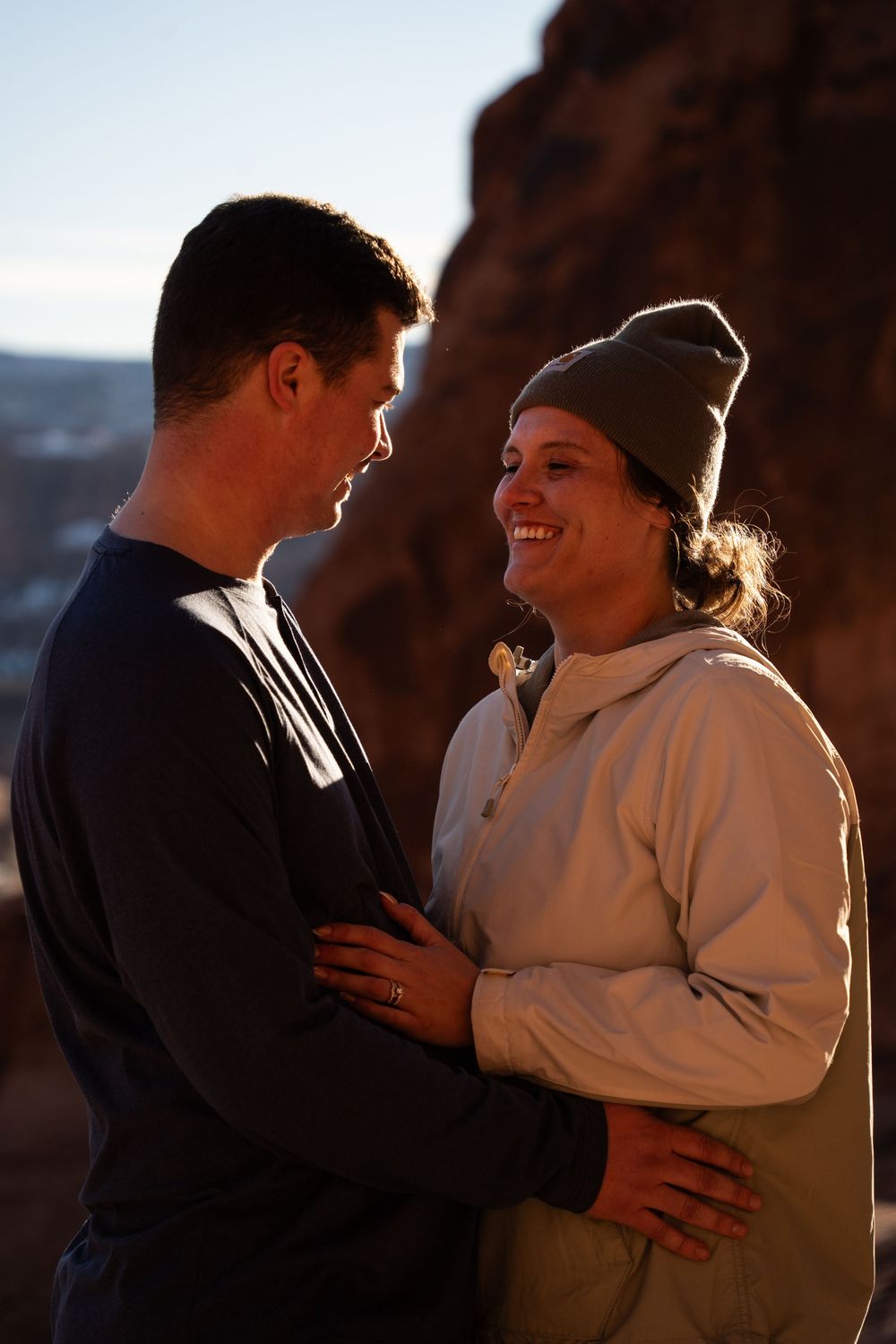 Couple embracing and smiling at sunset near Corona Arch