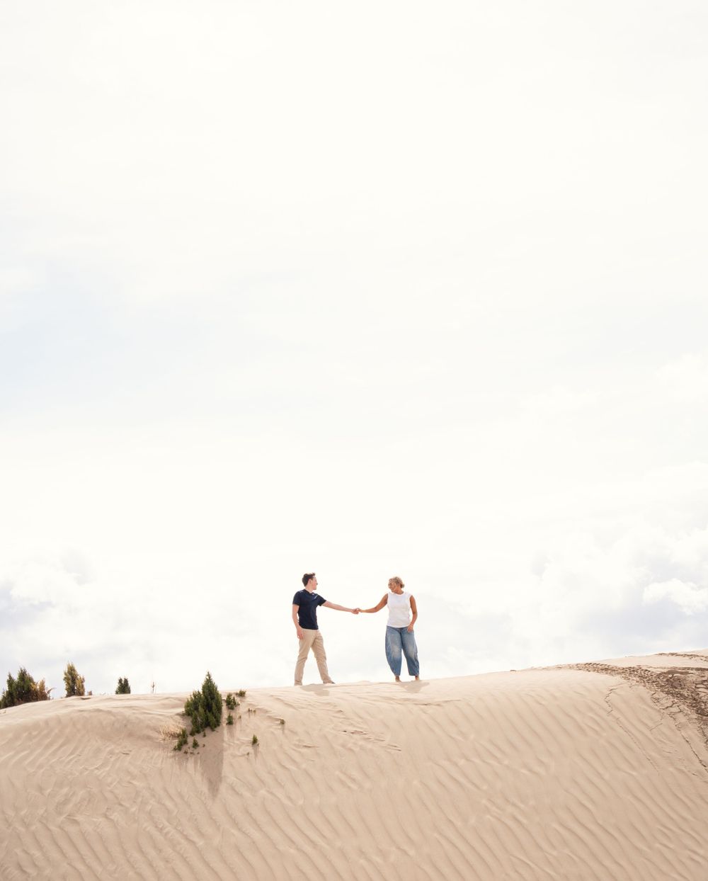 Engaged couple holding hands on top of a sand dune in Little Sahara