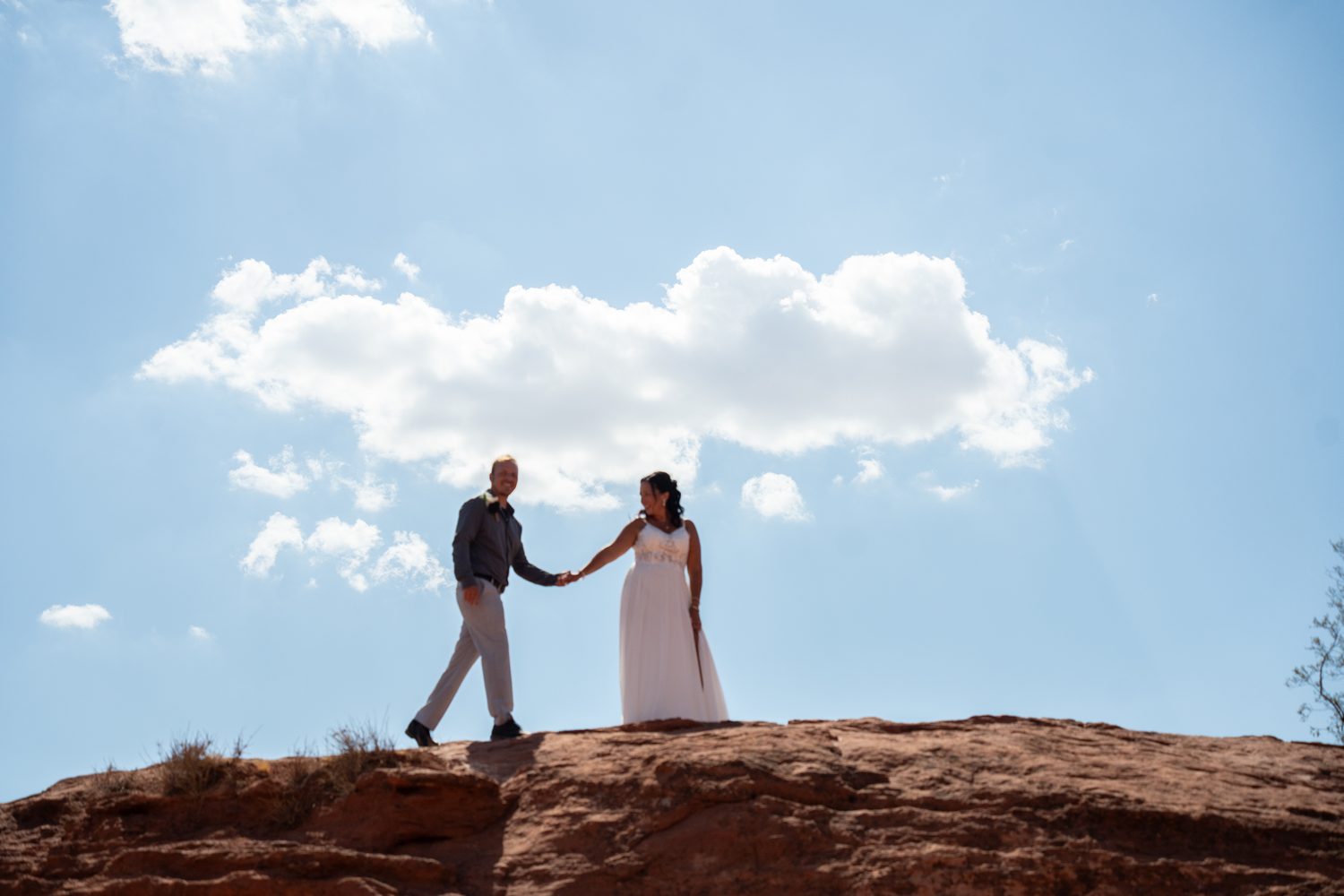 Bride and groom holding hands while walking along a red rock ridge during their St. George elopement