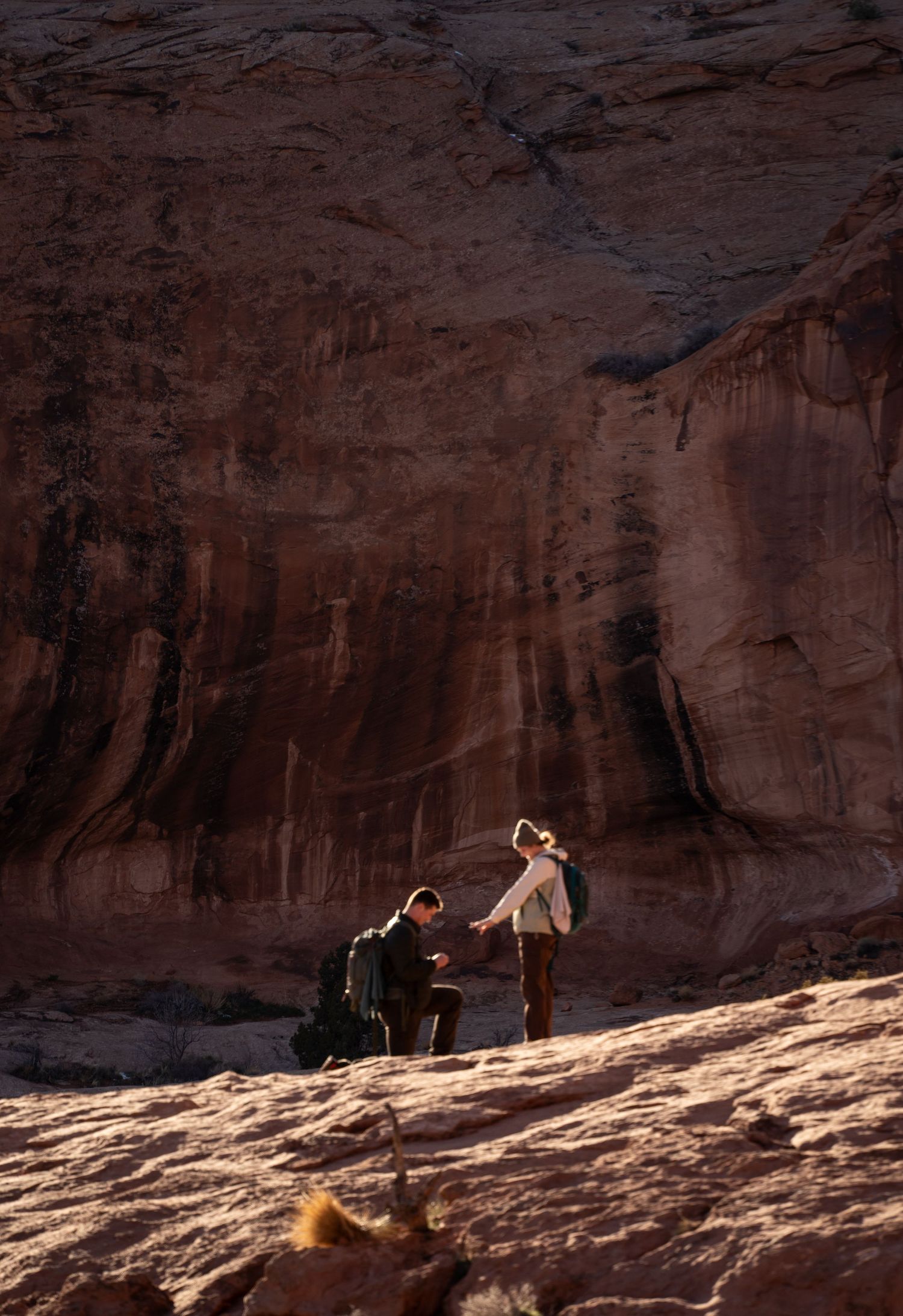 A romantic marriage proposal at Corona Arch, Moab, Utah, with a man on one knee before a woman against stunning sandstone cliffs