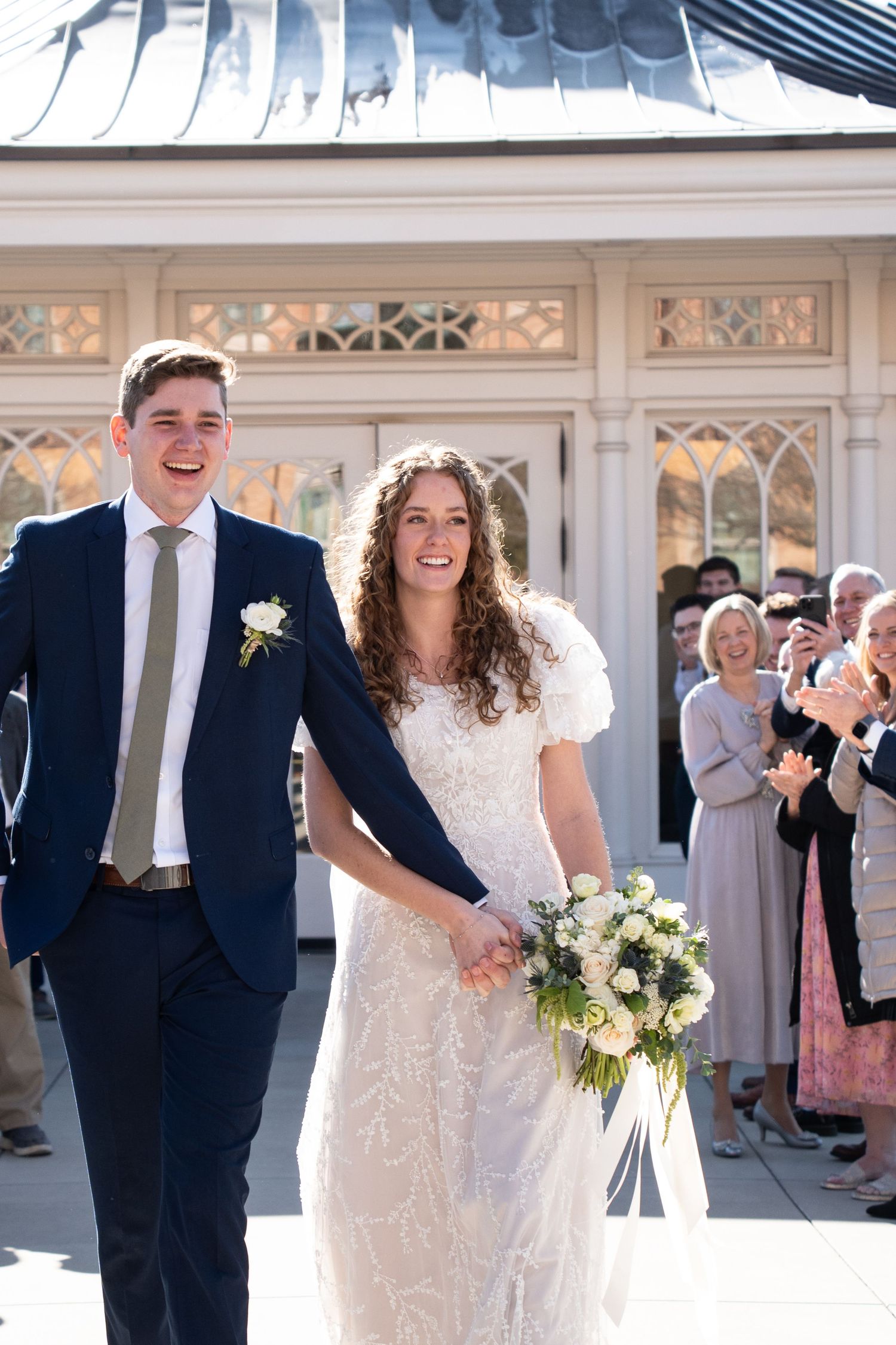 Laughing bride and groom exit Provo City Center Temple surrounded by family and friends on their wedding day
