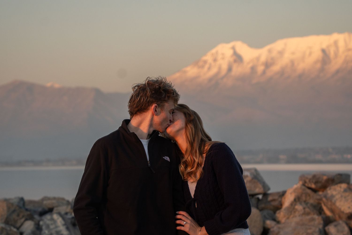 Couple sharing a romantic kiss at sunset with wasatch mountains and Utah lake in the background.