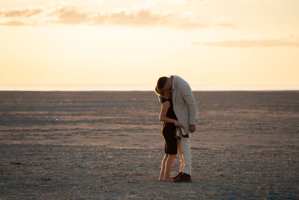 Couple celebrating on salt flats at sunset during a surprise proposal