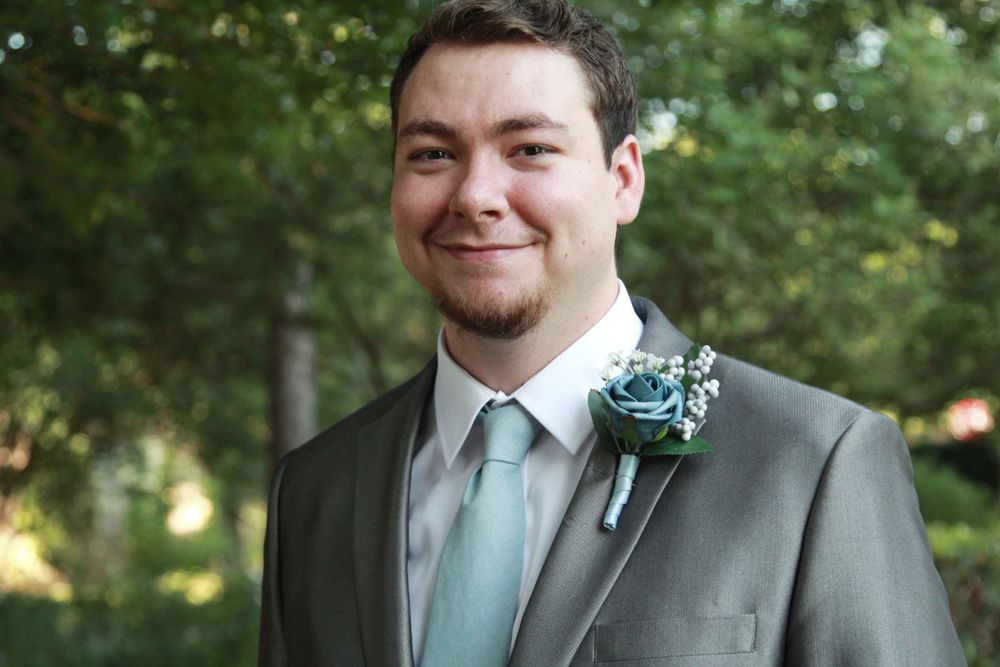 Young man in gray suit with teal tie and boutonniere smiling